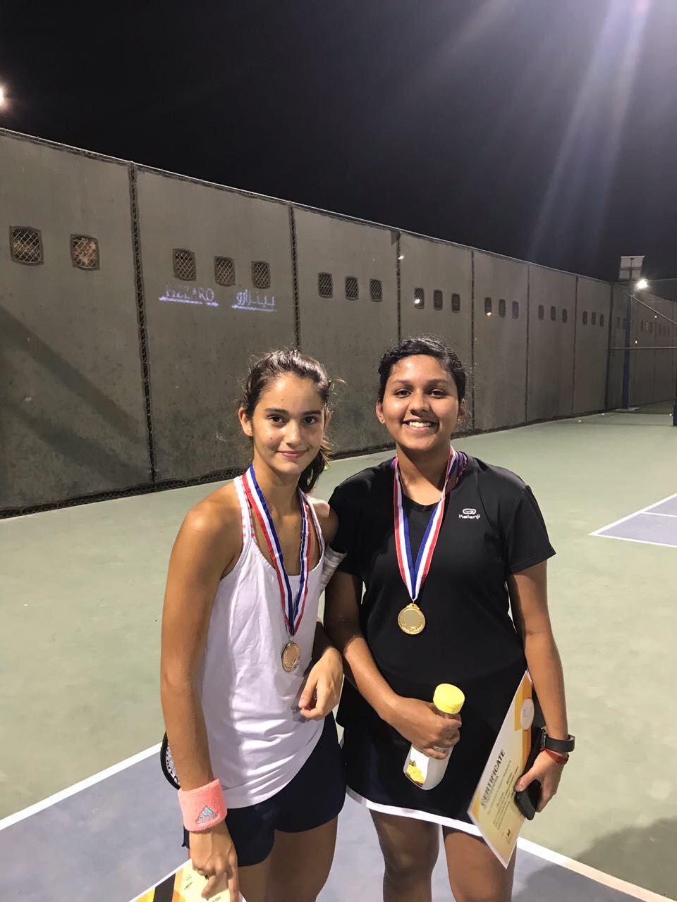 The author, Anjana, and a friend pose on a tennis court while wearing medallions.