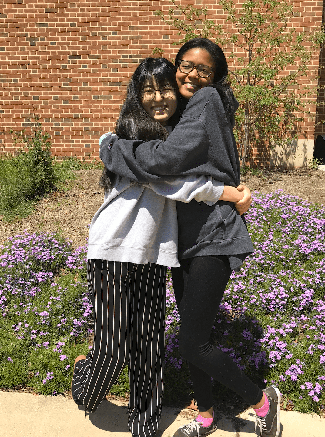 Zani and her friend hug while wearing an NYU sweater