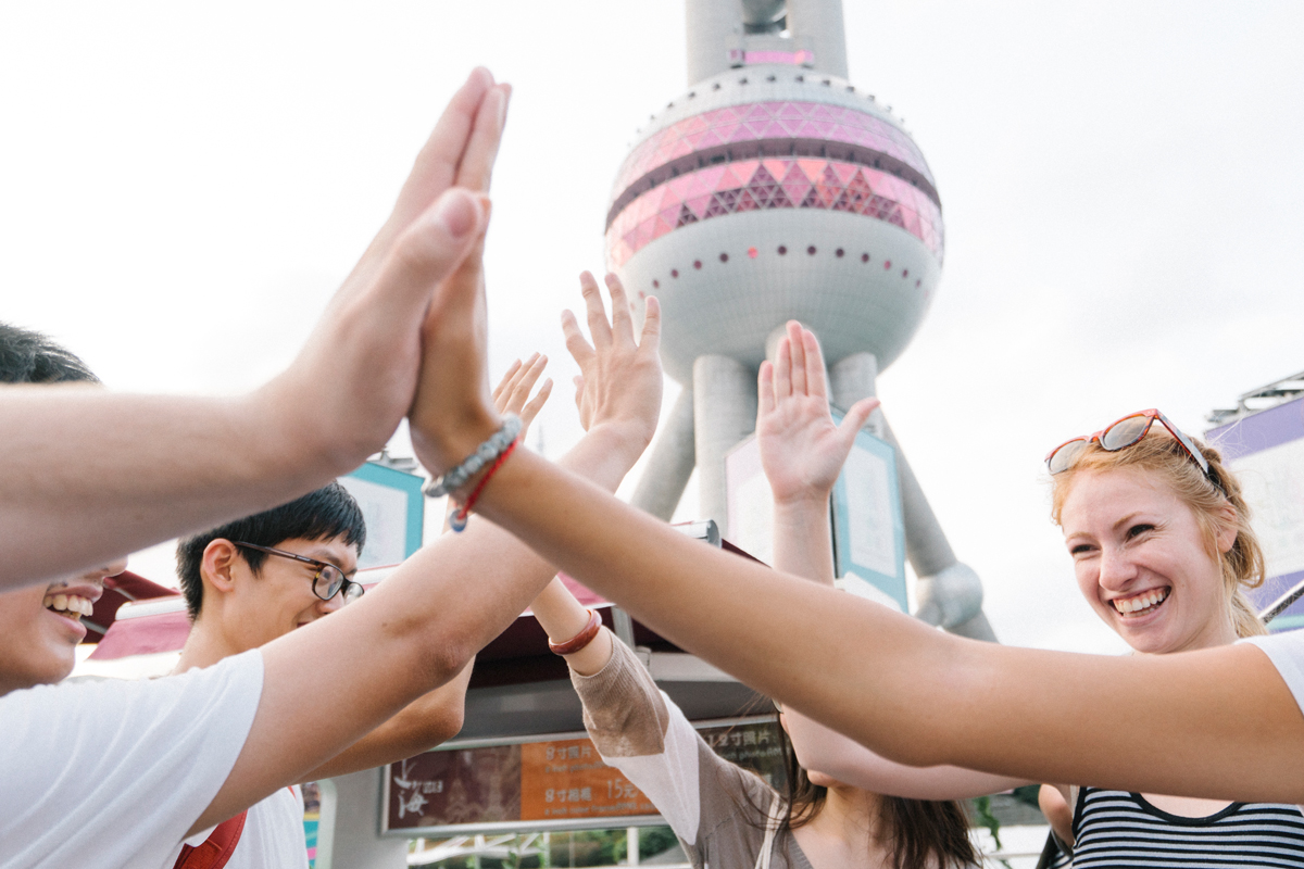 NYU Shanghai students smiling and cheering in front of the Oriental Pearl Tower.