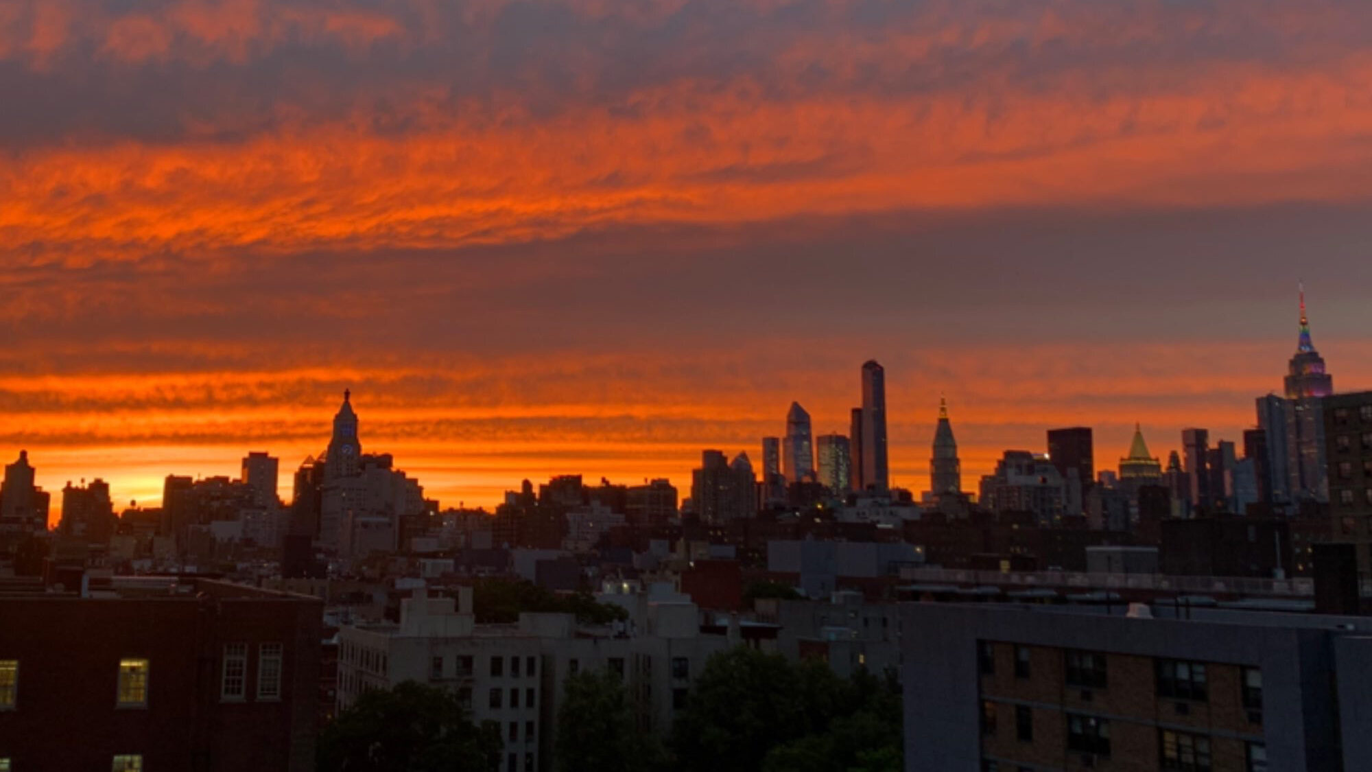The sun sets over rooftops in New York City.