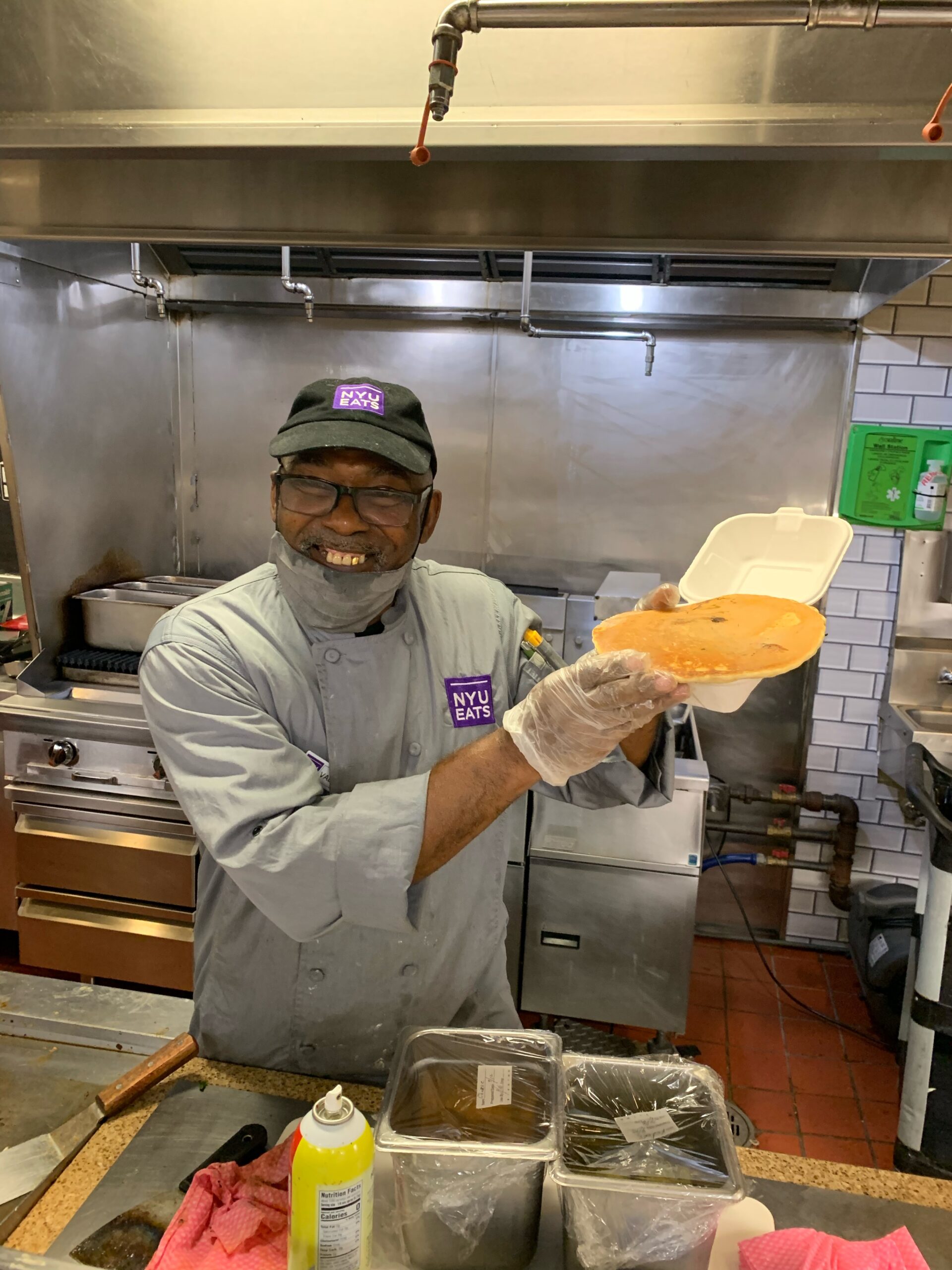 A dining hall staff member smiles while holding up a pancake.