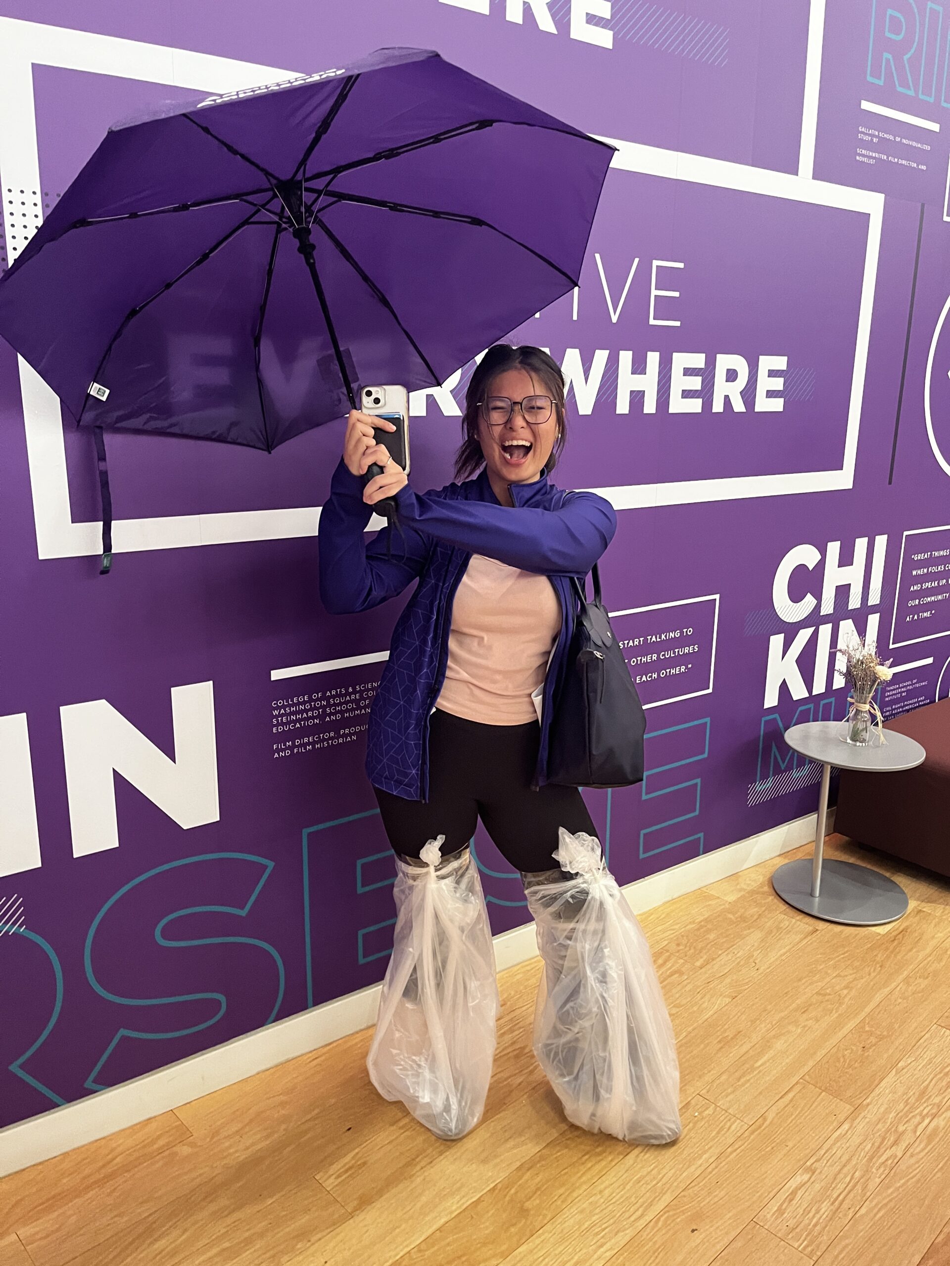 An NYU Admissions Ambassador holding an umbrella and wearing plastic sleeves over her shoes to prep for a tour in the rain.