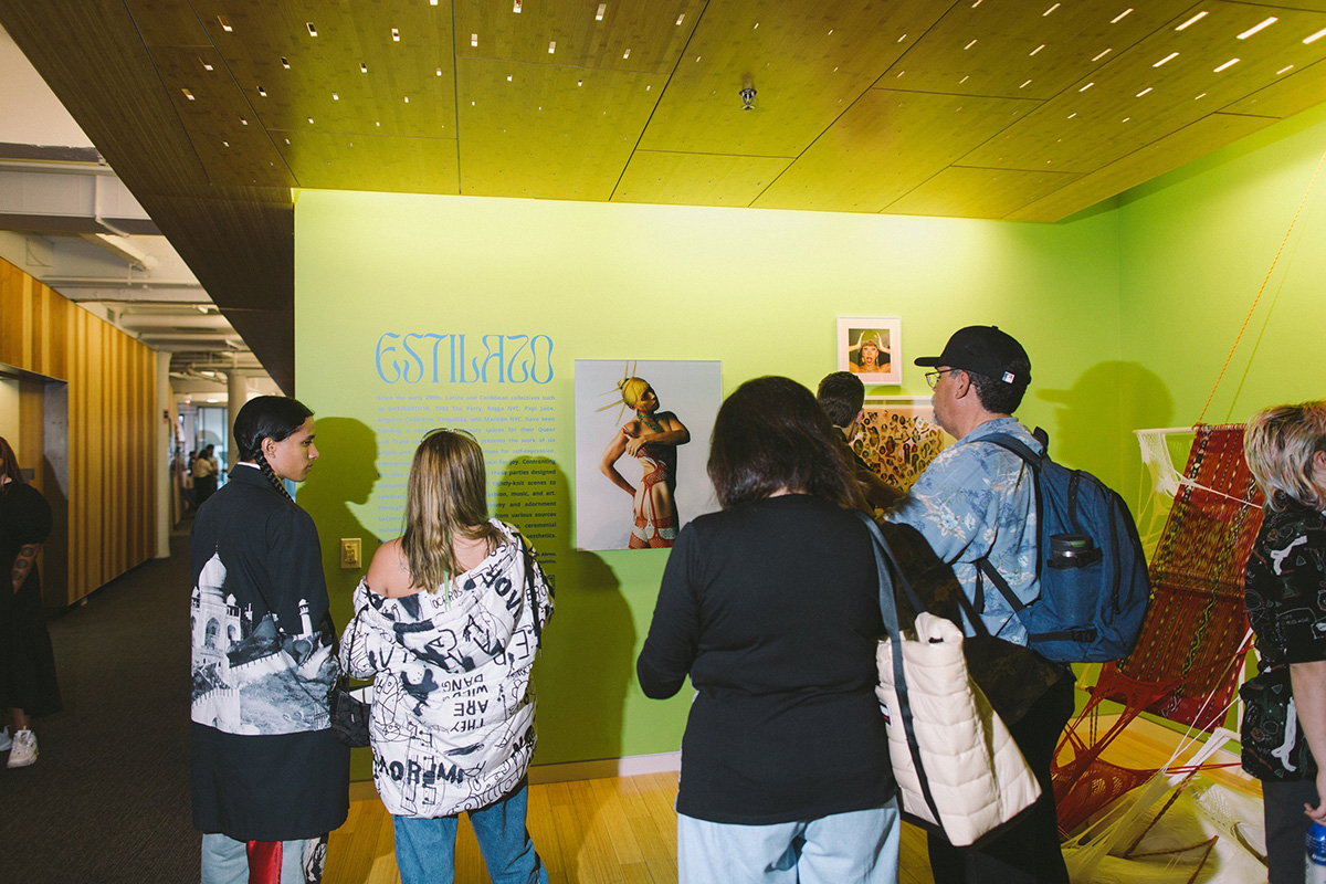 Exhibition view of Estilazo featuring artwork from Angel Añazco being viewed by a group of individuals.