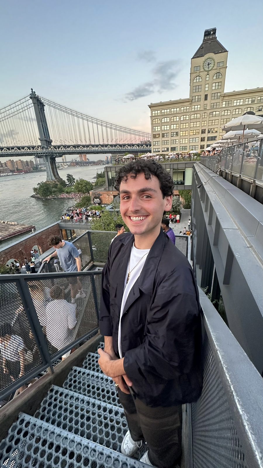 Myself smiling, standing on some stairs with the Brooklyn bridge in the background
