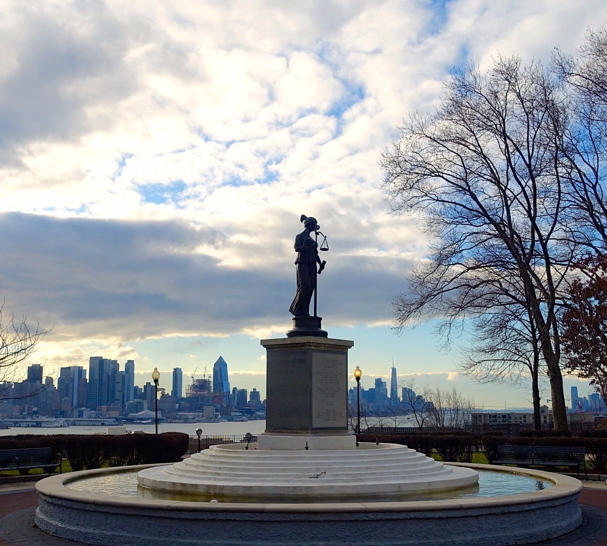 A statue in a park overlooking the New York City skyline.
