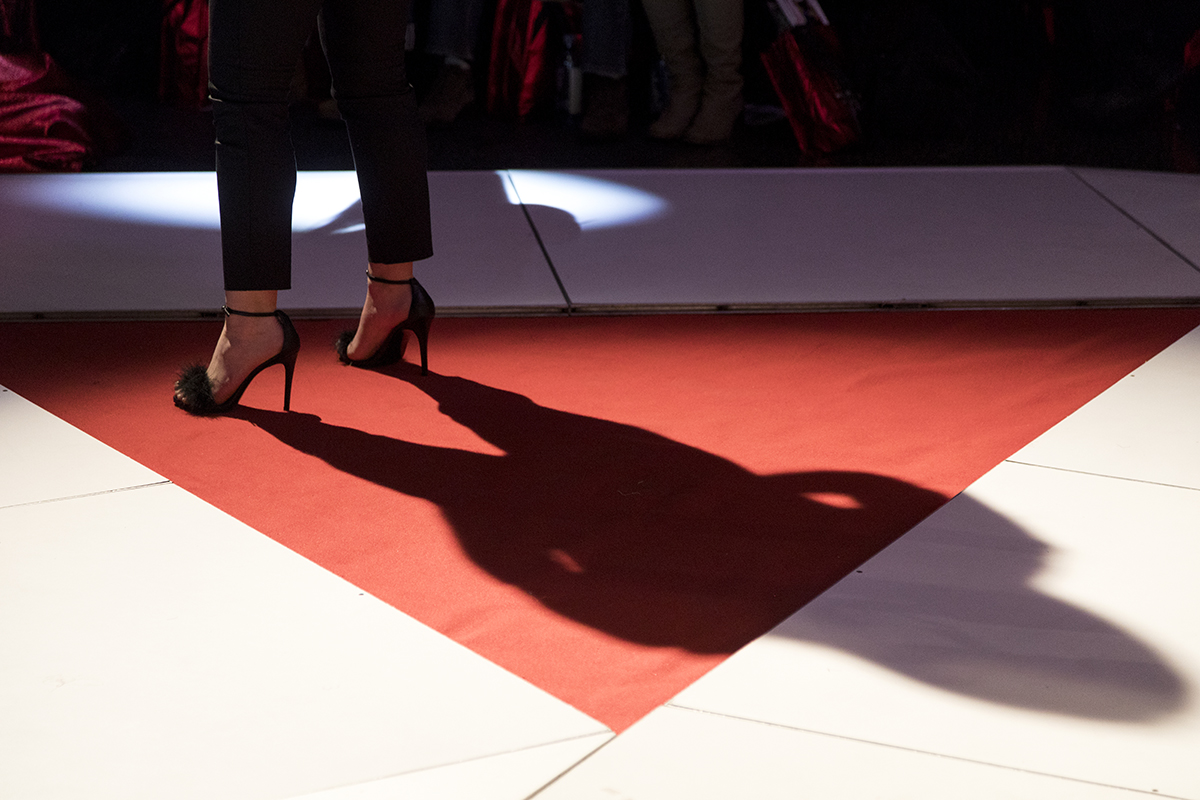 The shadow of a model wearing black high heels on a runway.
