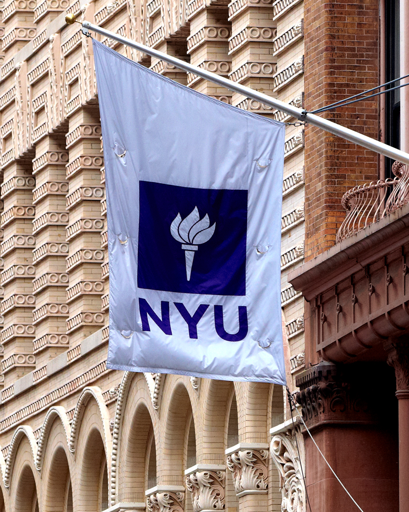A white and violet NYU flag hanging from a building.