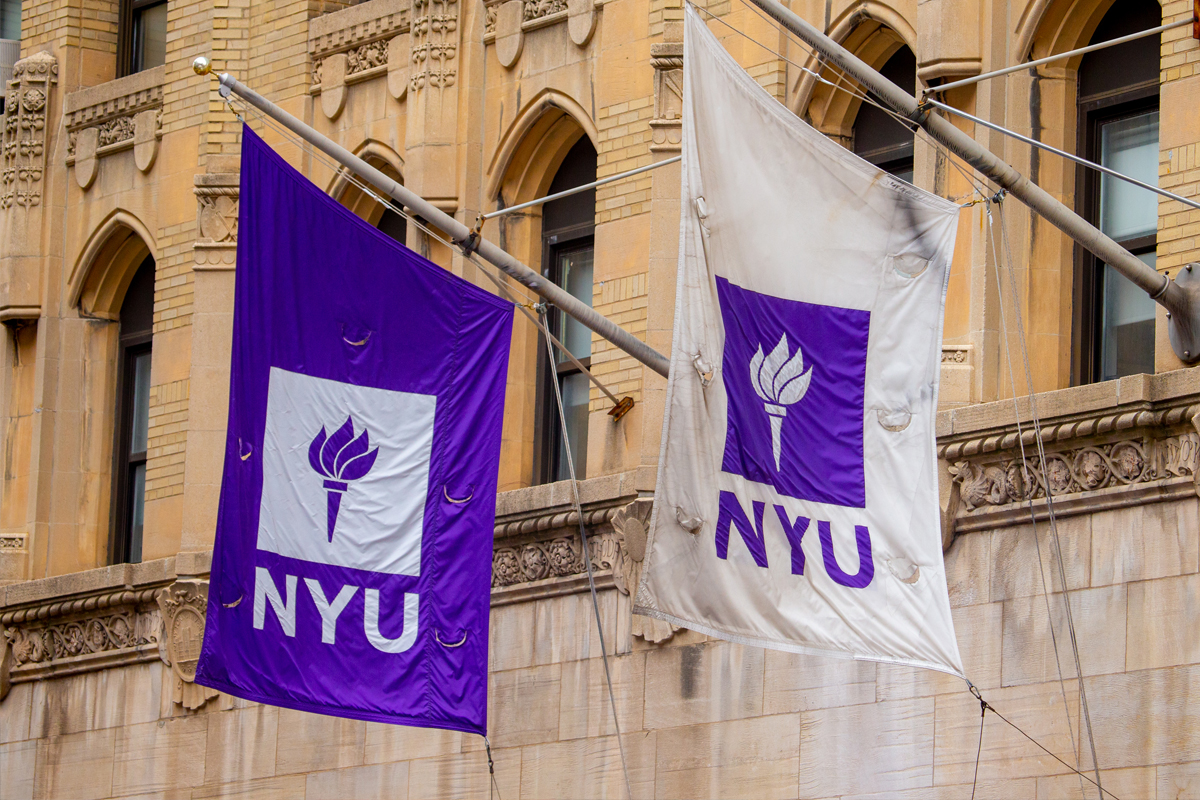 Two NYU flags, one violet and white and the other white and violet, hang from a building.