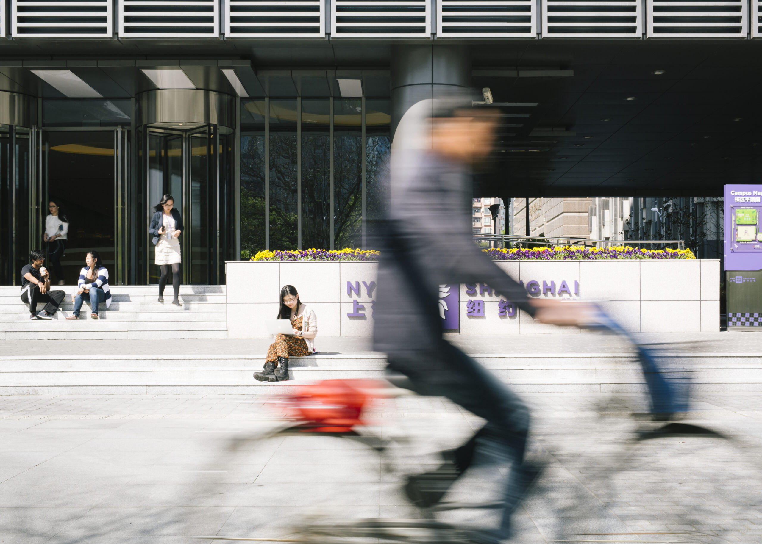 Exterior of a building on the NYU Shanghai campus. A blurry biker rides by.