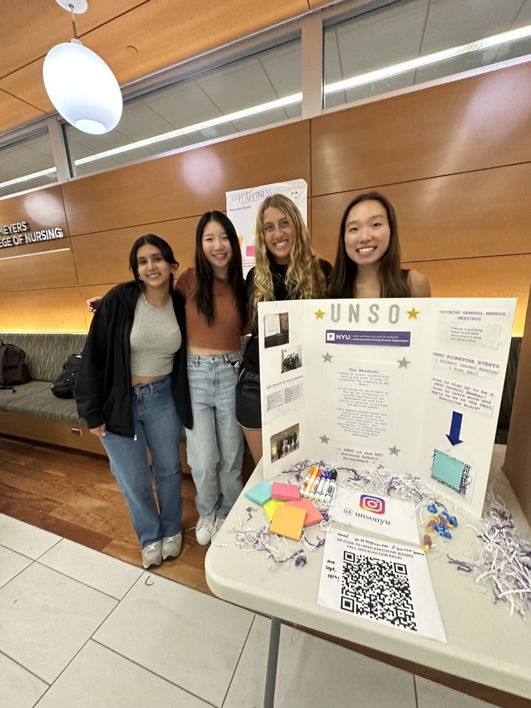 Nursing students standing in front of a poster board positioned on a table at a club fair.