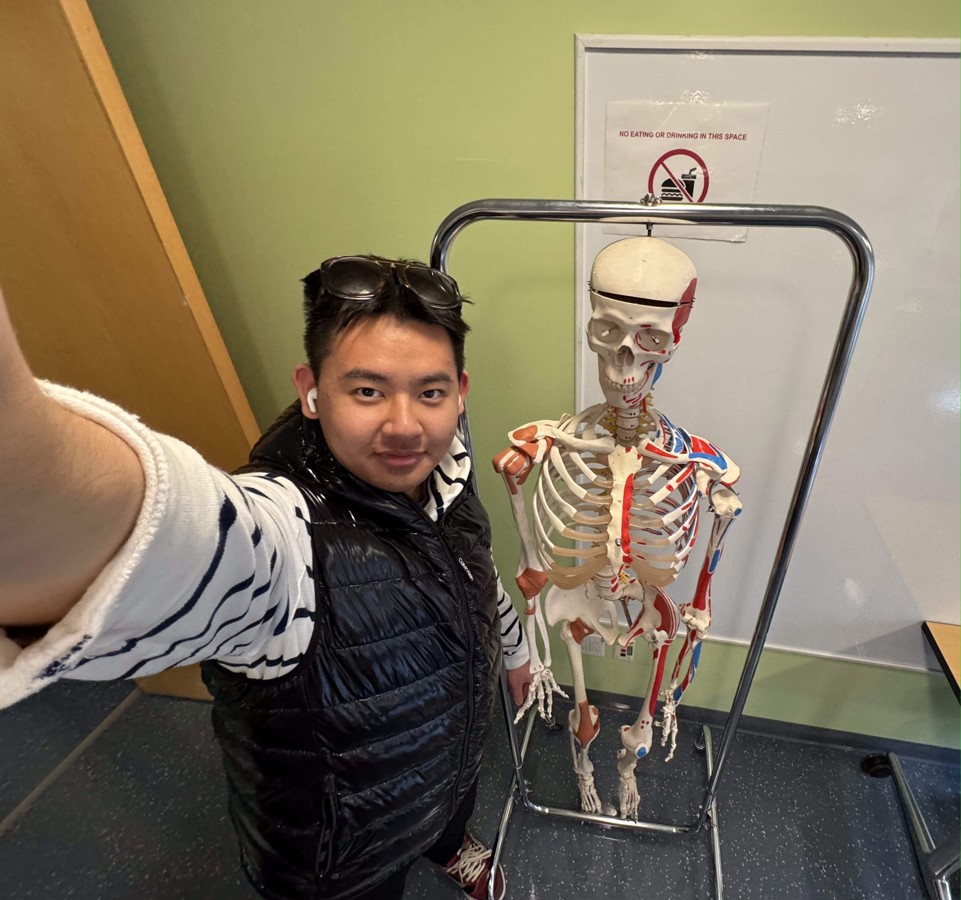 Andrew Wang poses for a selfie next to a model skeleton