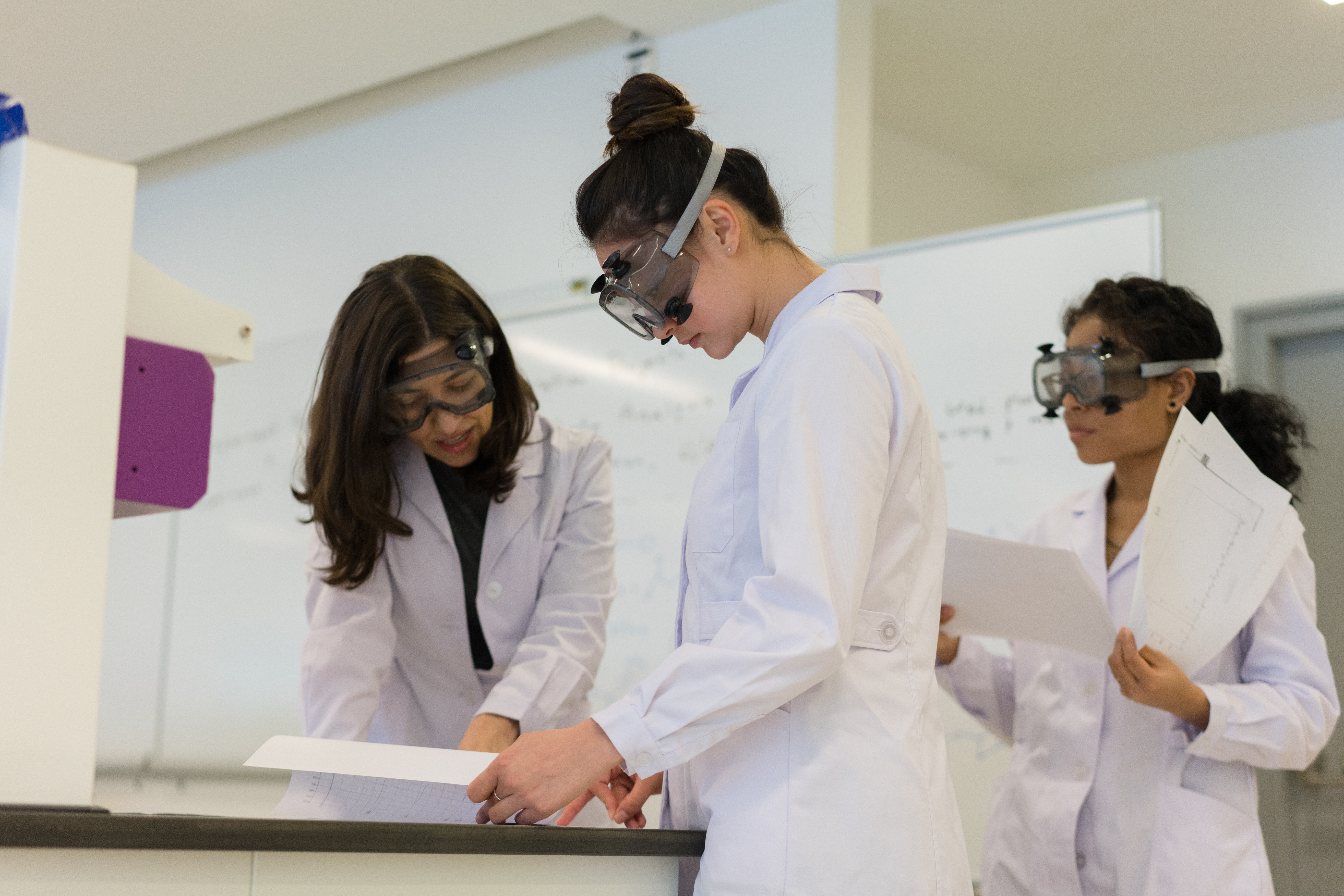 Two female-presenting students and a female-presenting professor working in a lab together.