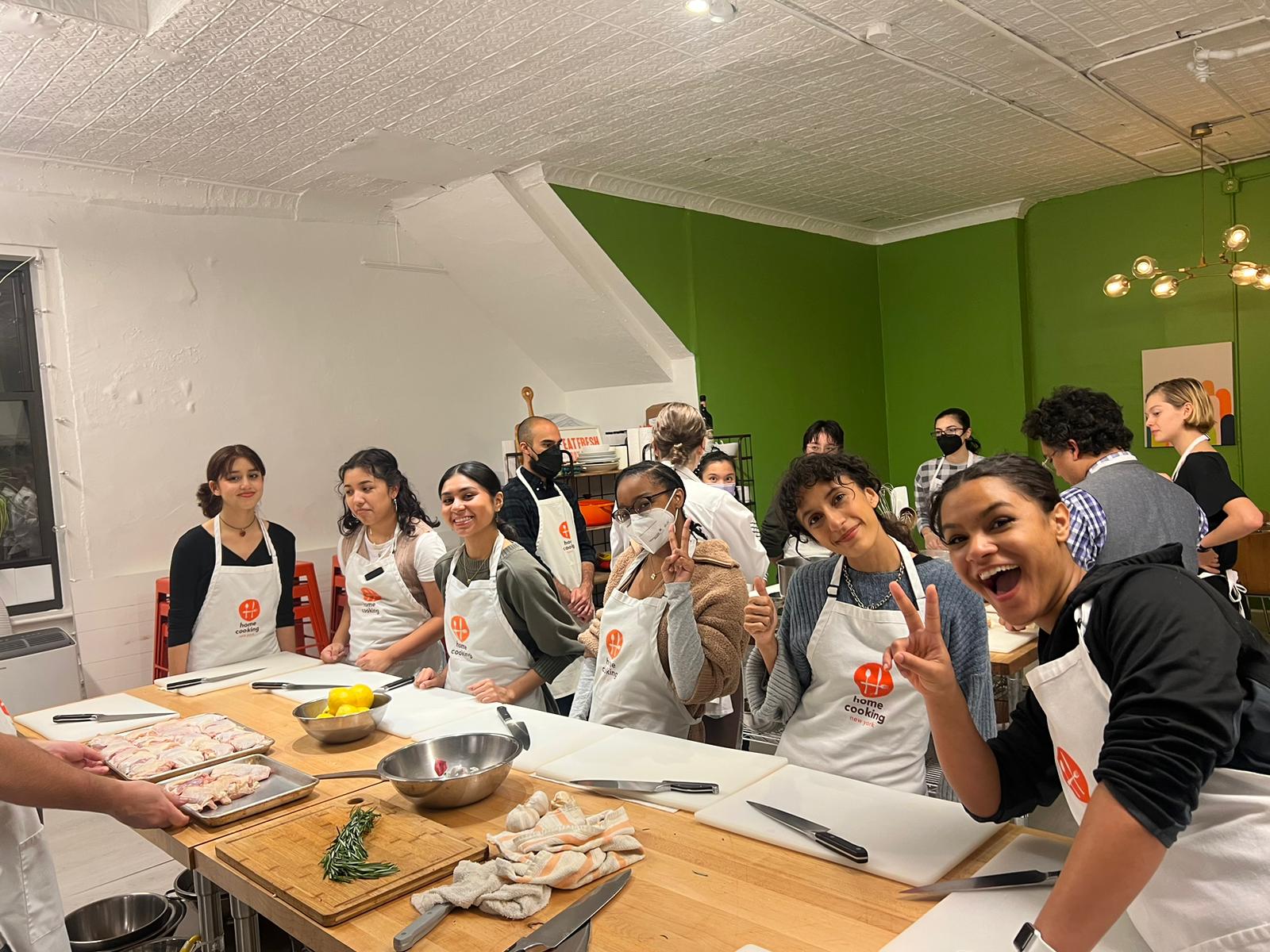 Students of color taking a cooking class. All are wearing aprons.