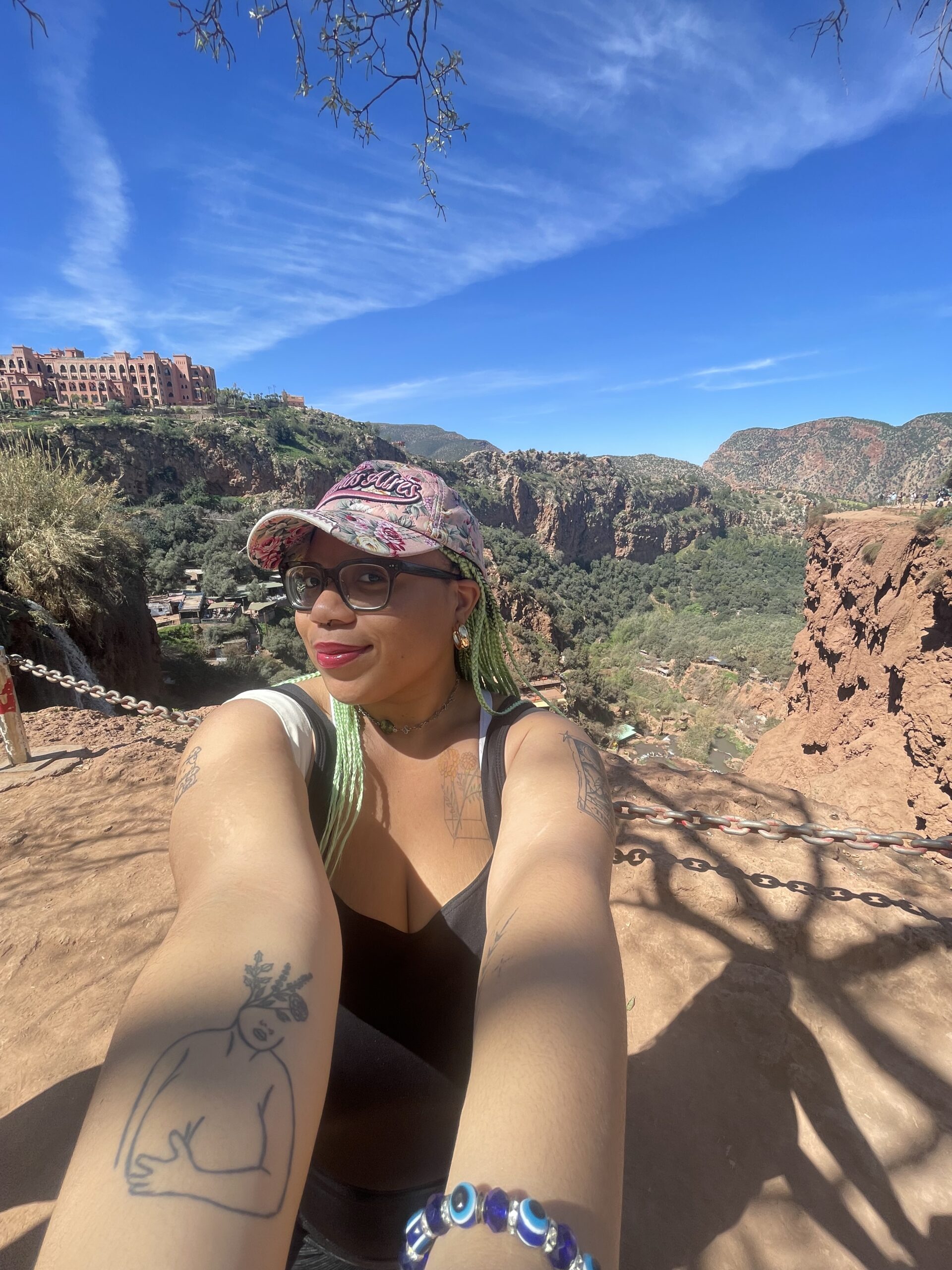 A Black woman, wearing a hat that reads “Buenos Aires,” takes a selfie in front of a mountainous backdrop.