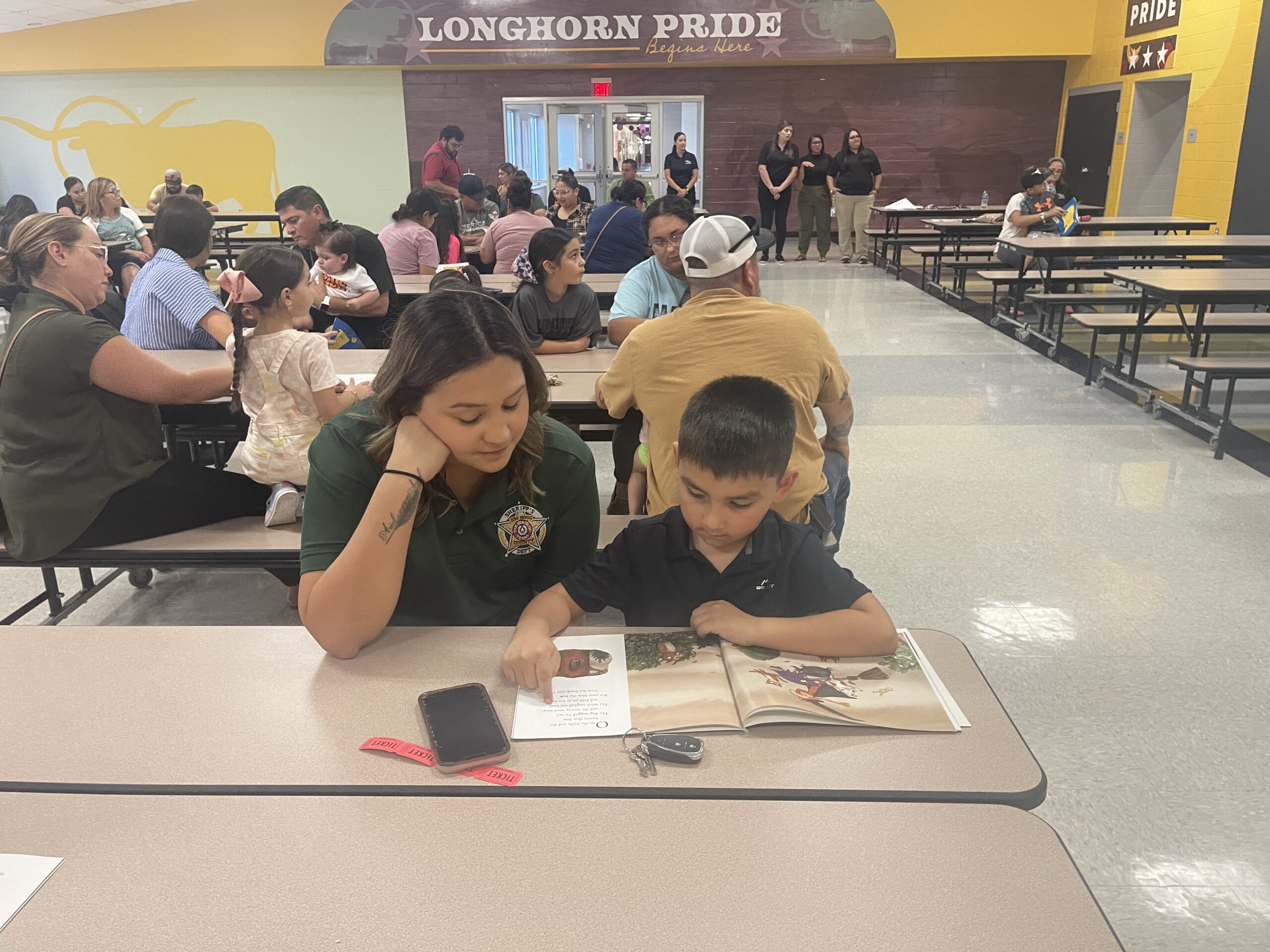 A female-presenting high schooler reads with a male-presenting elementary school child.