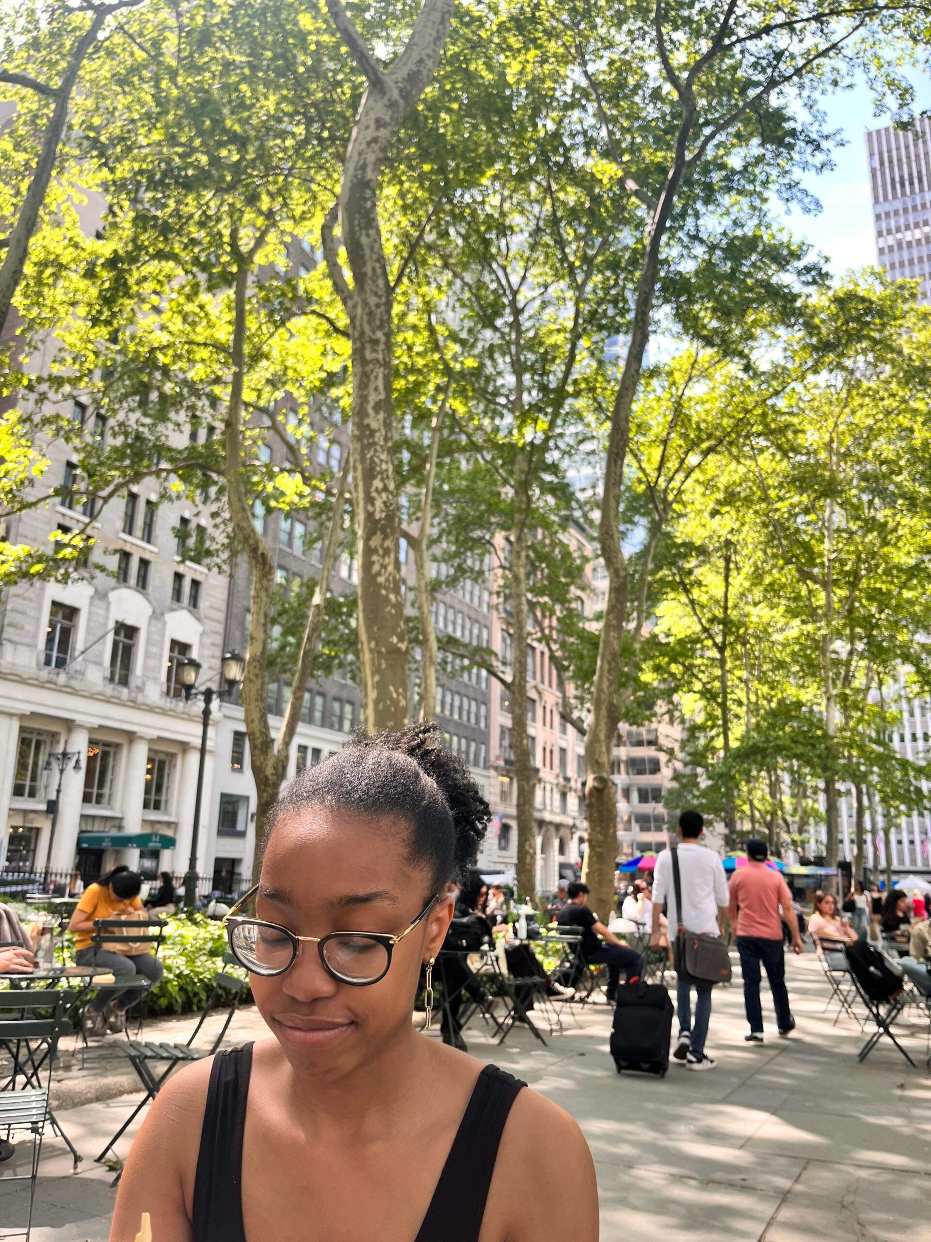 A woman of color wearing glasses sits at a table in a New York City park.