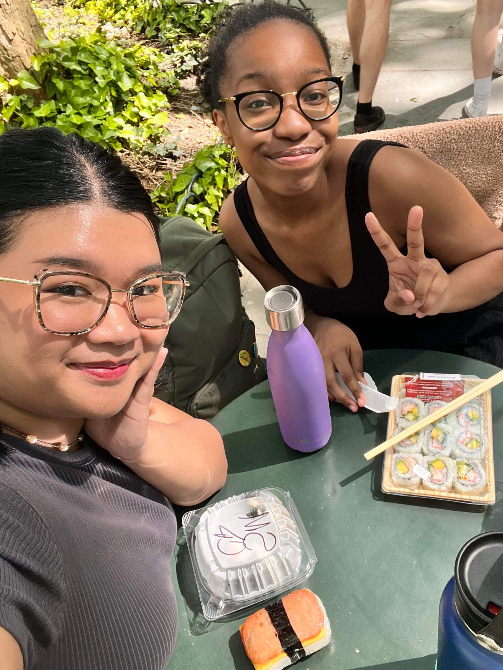 Two women of color eating sushi at a table in a New York City park.