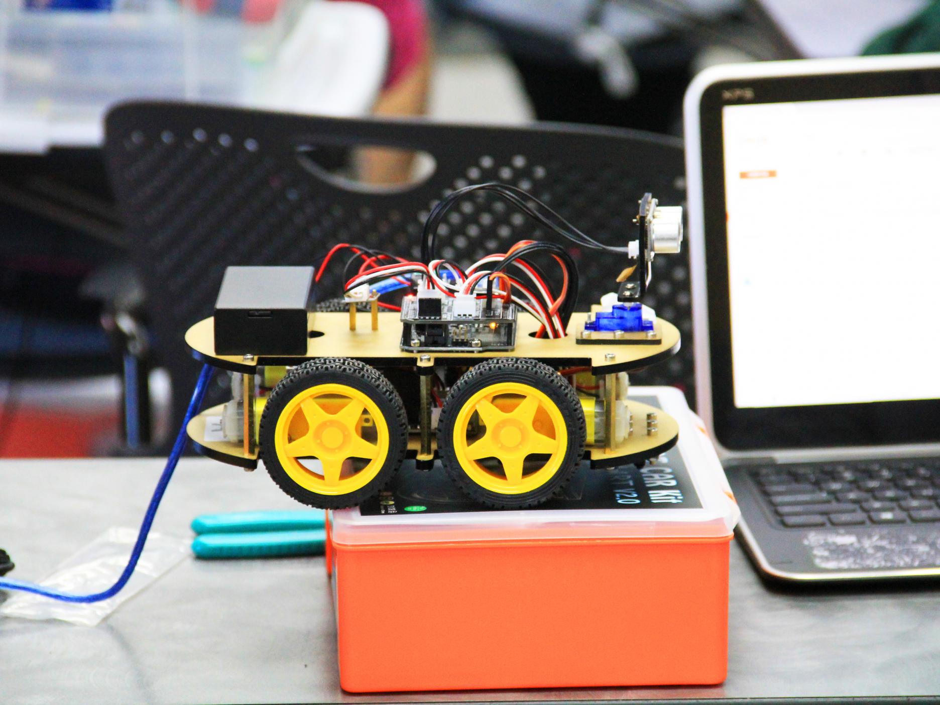A small yellow robotic car sits on top of a work station.
