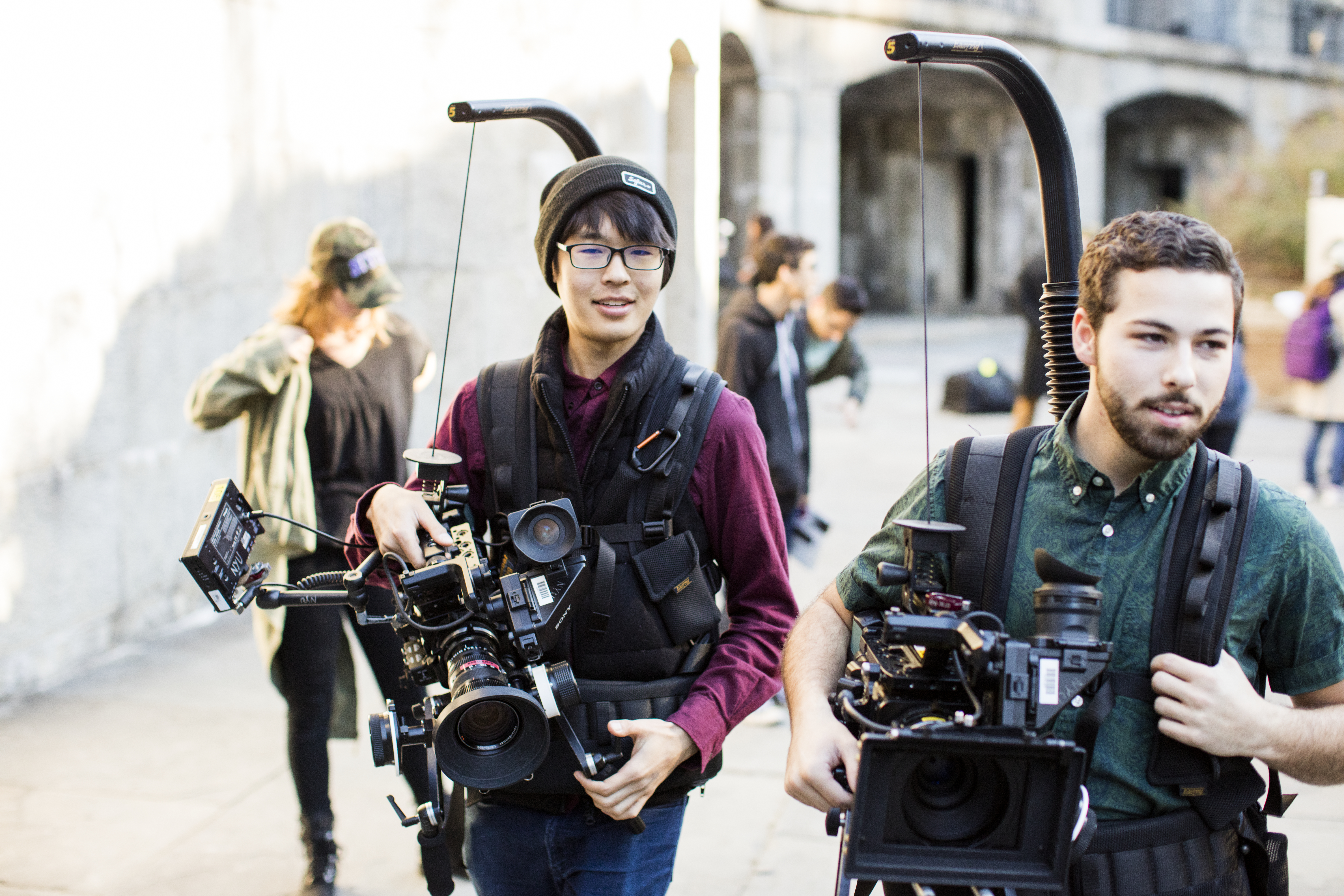 Two male-presenting students carrying large cameras.