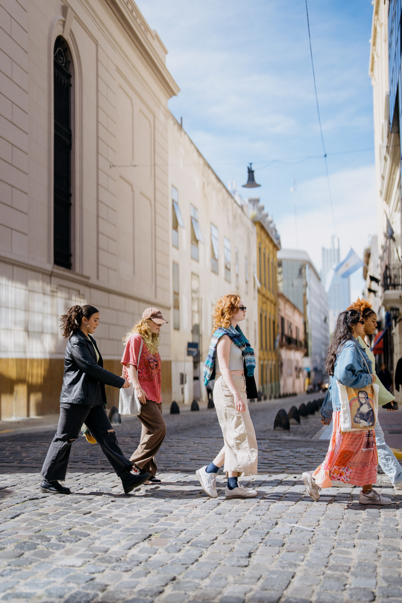 A group of female-presenting study away students walk across a cobblestone street in Buenos Aires.