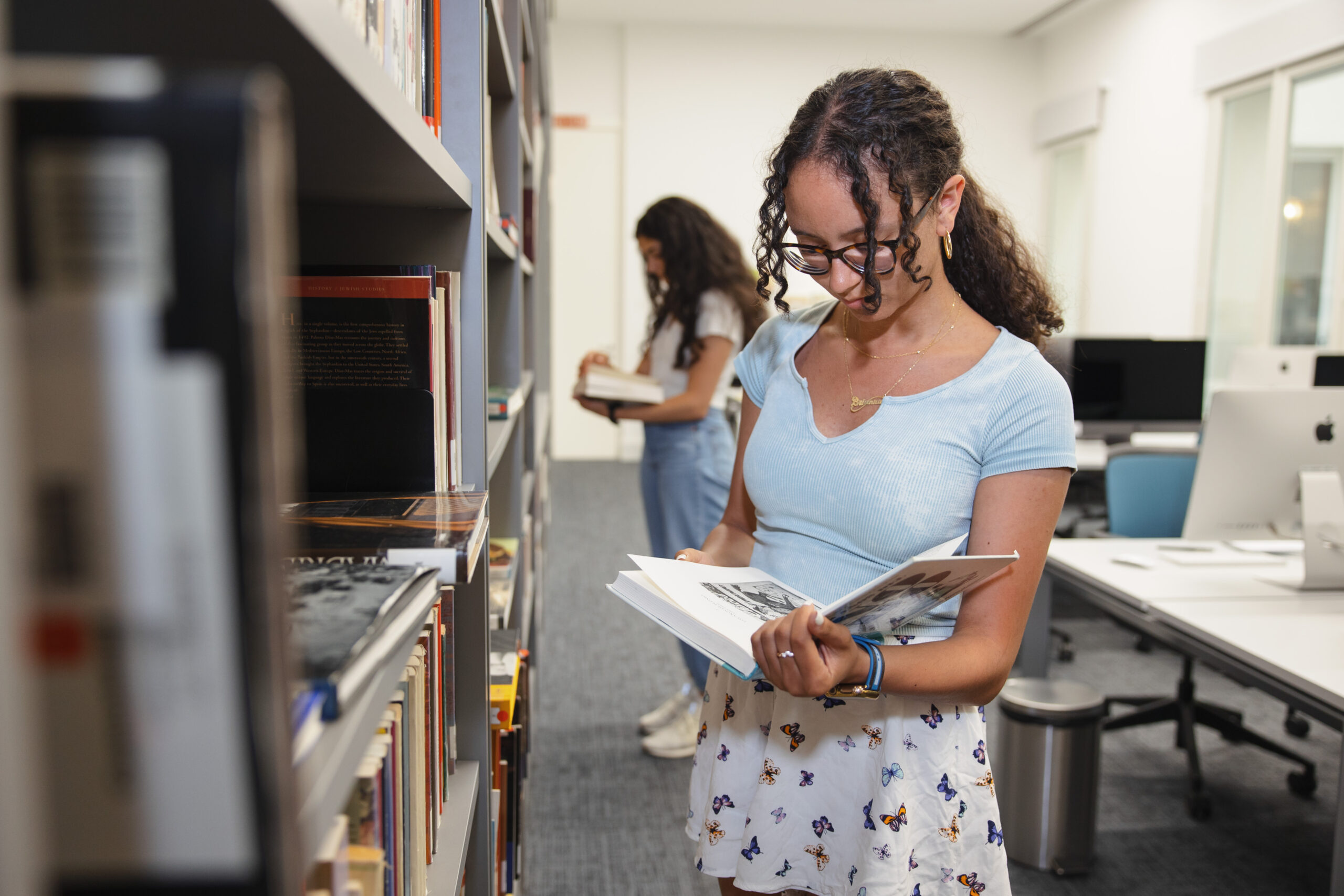 A female-presenting student browsing a book in a library.