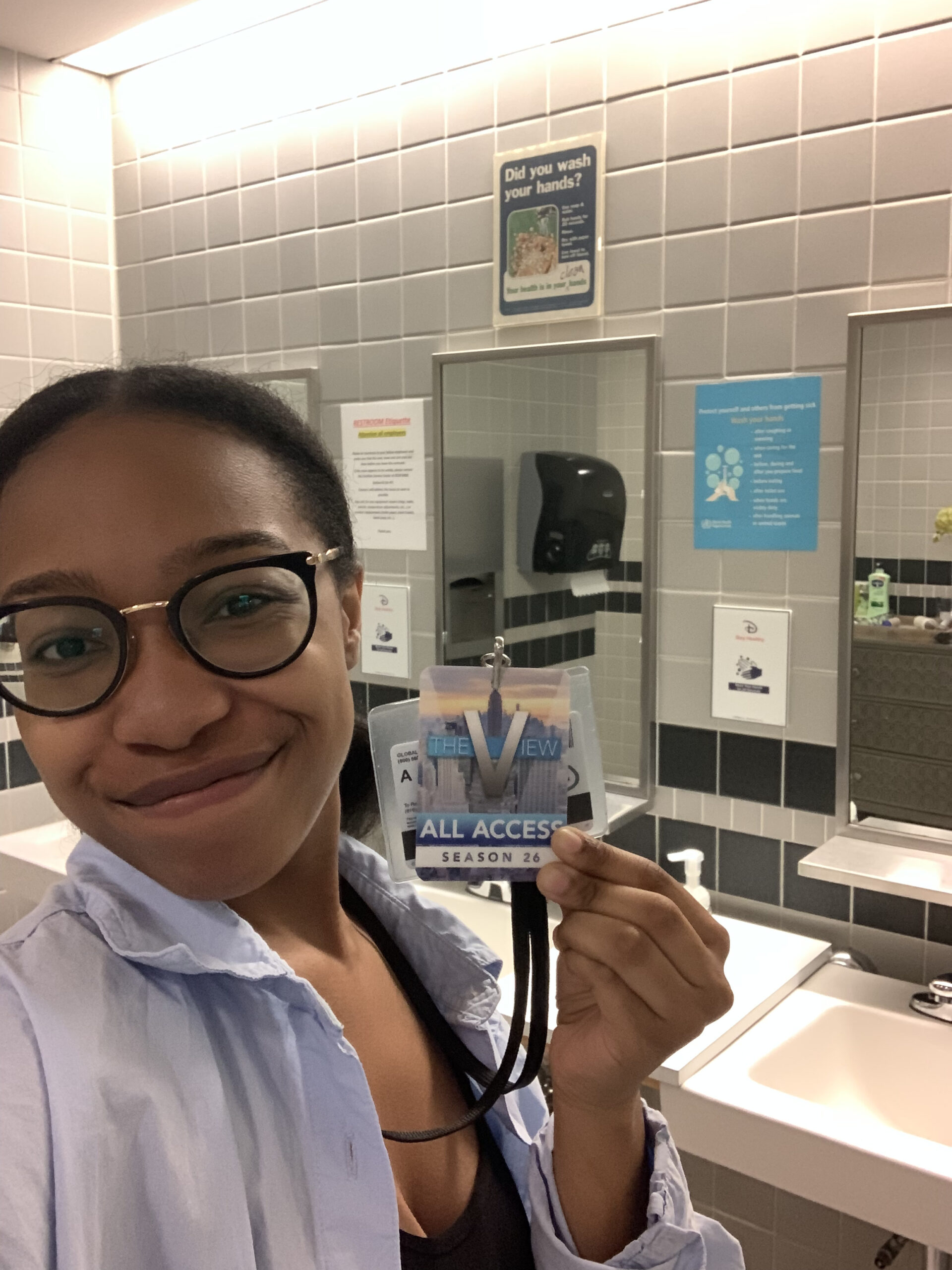 The author smiling in a bathroom while holding up her all access pass to The View.