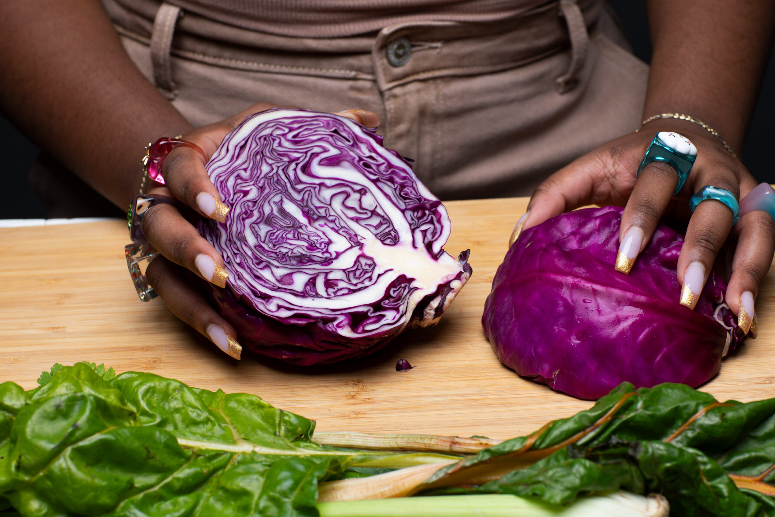 Hands holding a red cabbage that has been split in two on a cutting board.