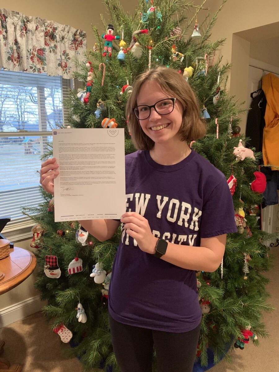 Student holding NYU acceptance letter standing in front of a Christmas tree.