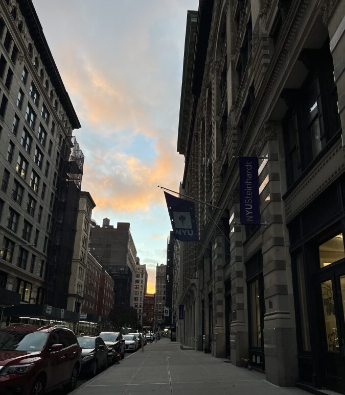 Pink and blue sky peeks through New York City buildings as the sun sets.