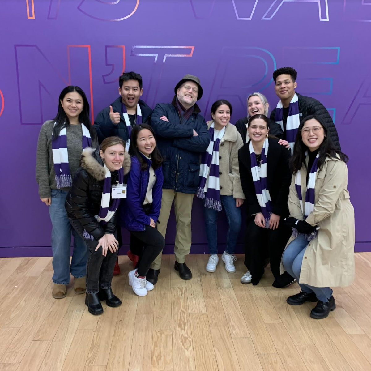 Admissions Ambassadors smiling for the camera in front of an NYU Violet wall.