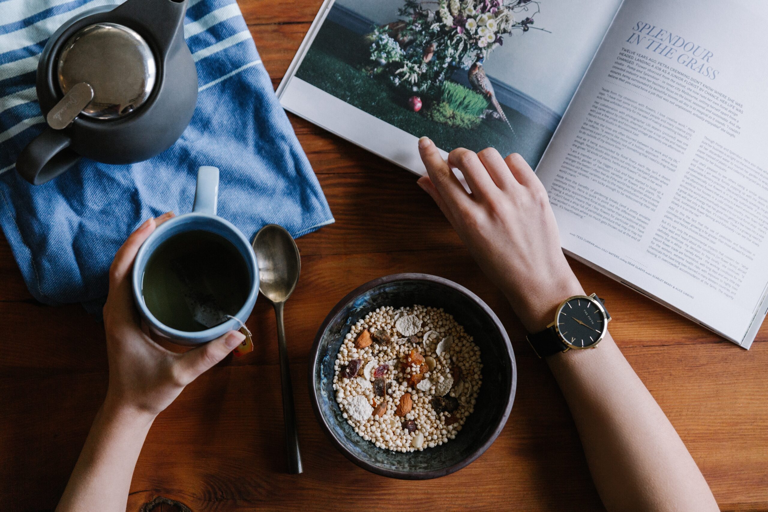 A person holding a coffee cup and enjoying a bowl of cereal while reading a book.