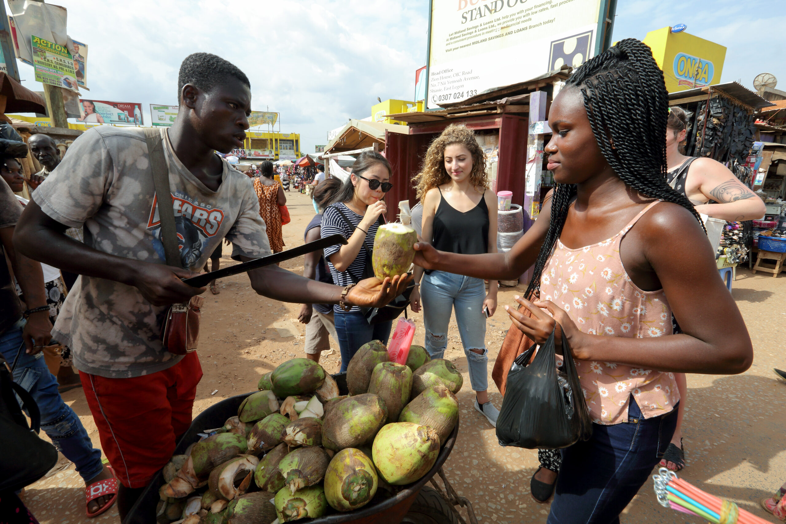 A female-presenting student of color purchases cut coconut from a vendor in Ghana, Accra.