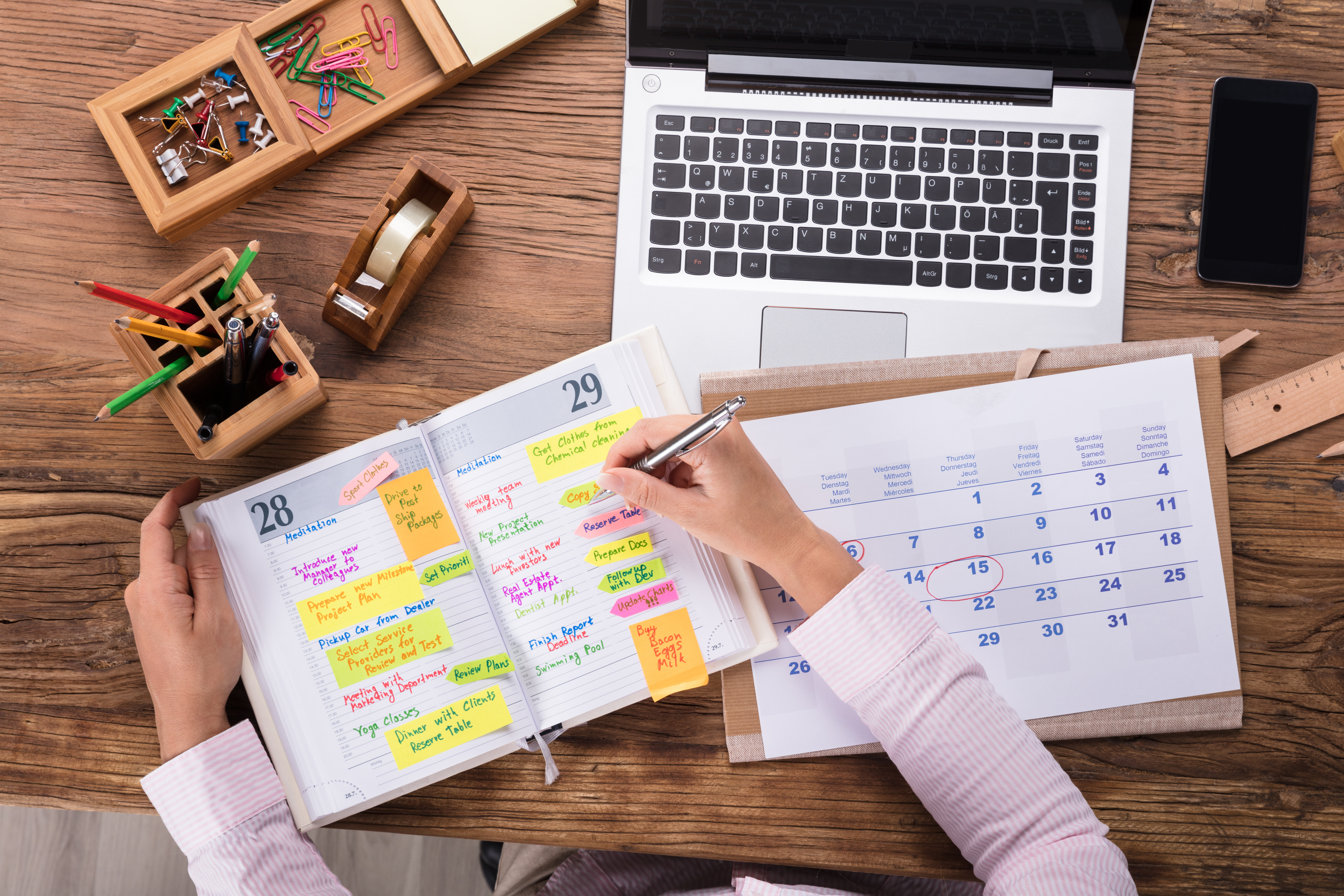 A person sits at a desk, planning their schedule in an organizer and calendar.