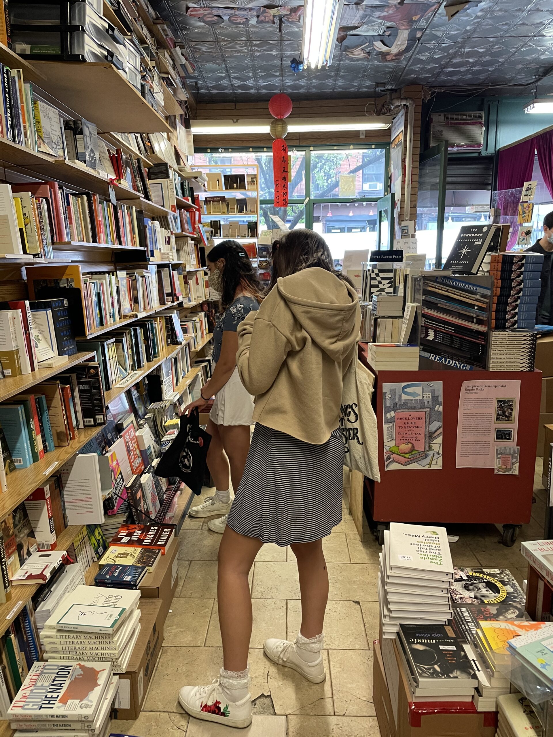 Two female-presenting students browse shelves of books in a used bookstore.