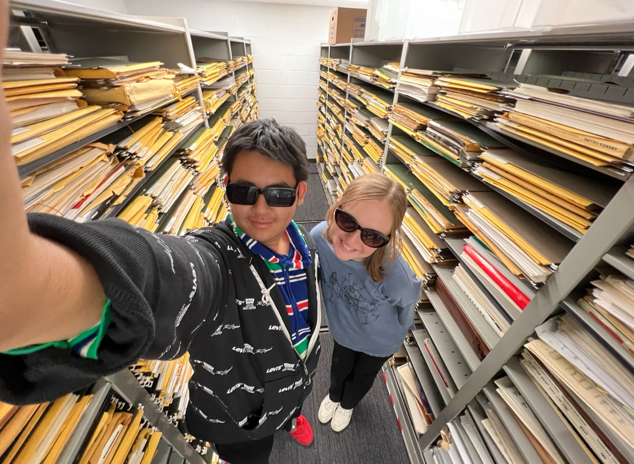 Andrew and another student posing in the library stacks for a selfie.