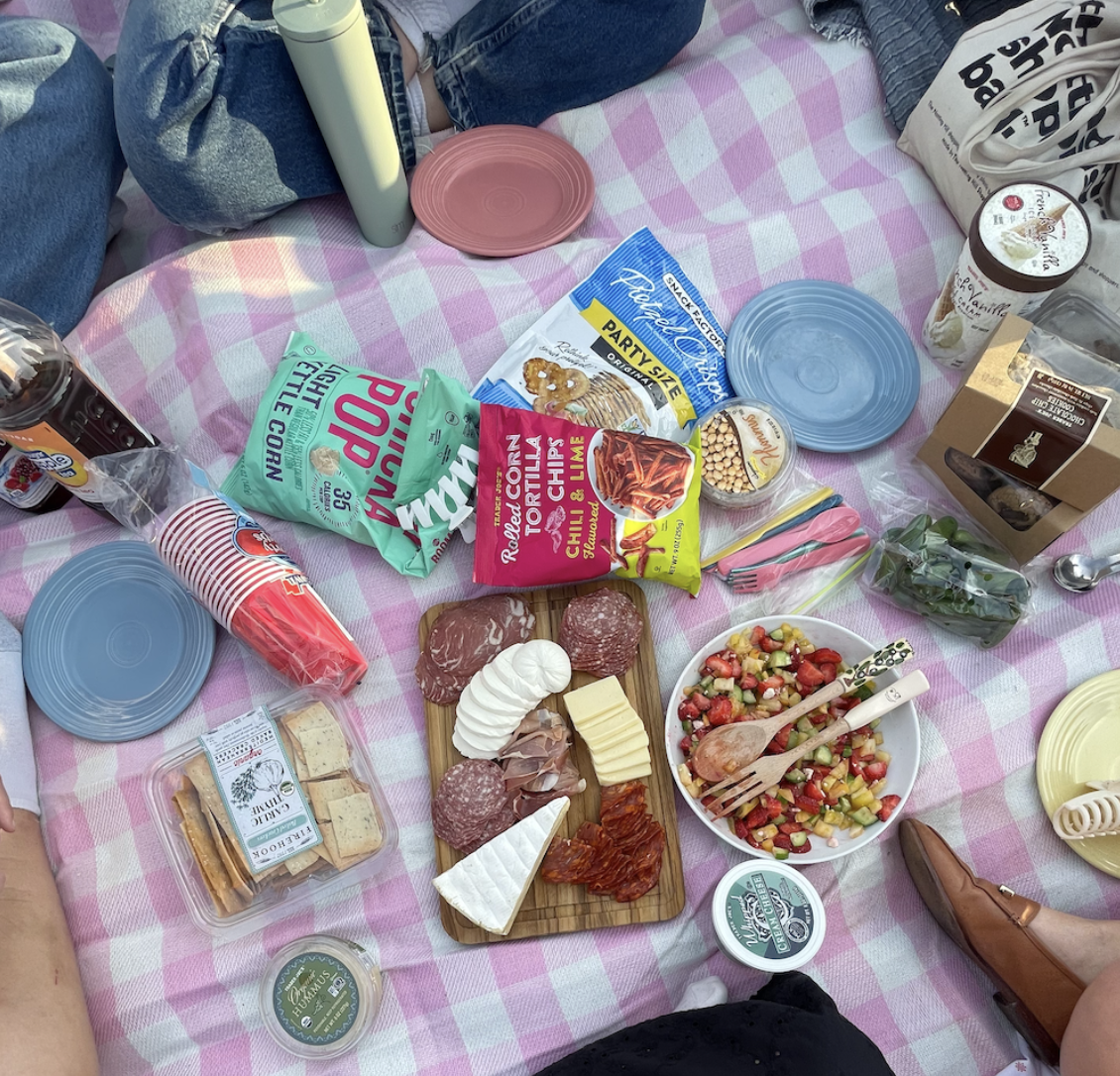 Cheese, snacks, and plates on a picnic blanket.