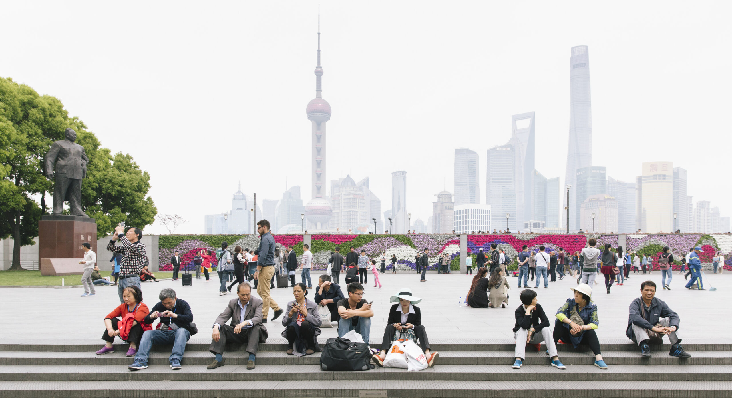 People sitting and relaxing in a public square with the Shanghai skyline in the distance.