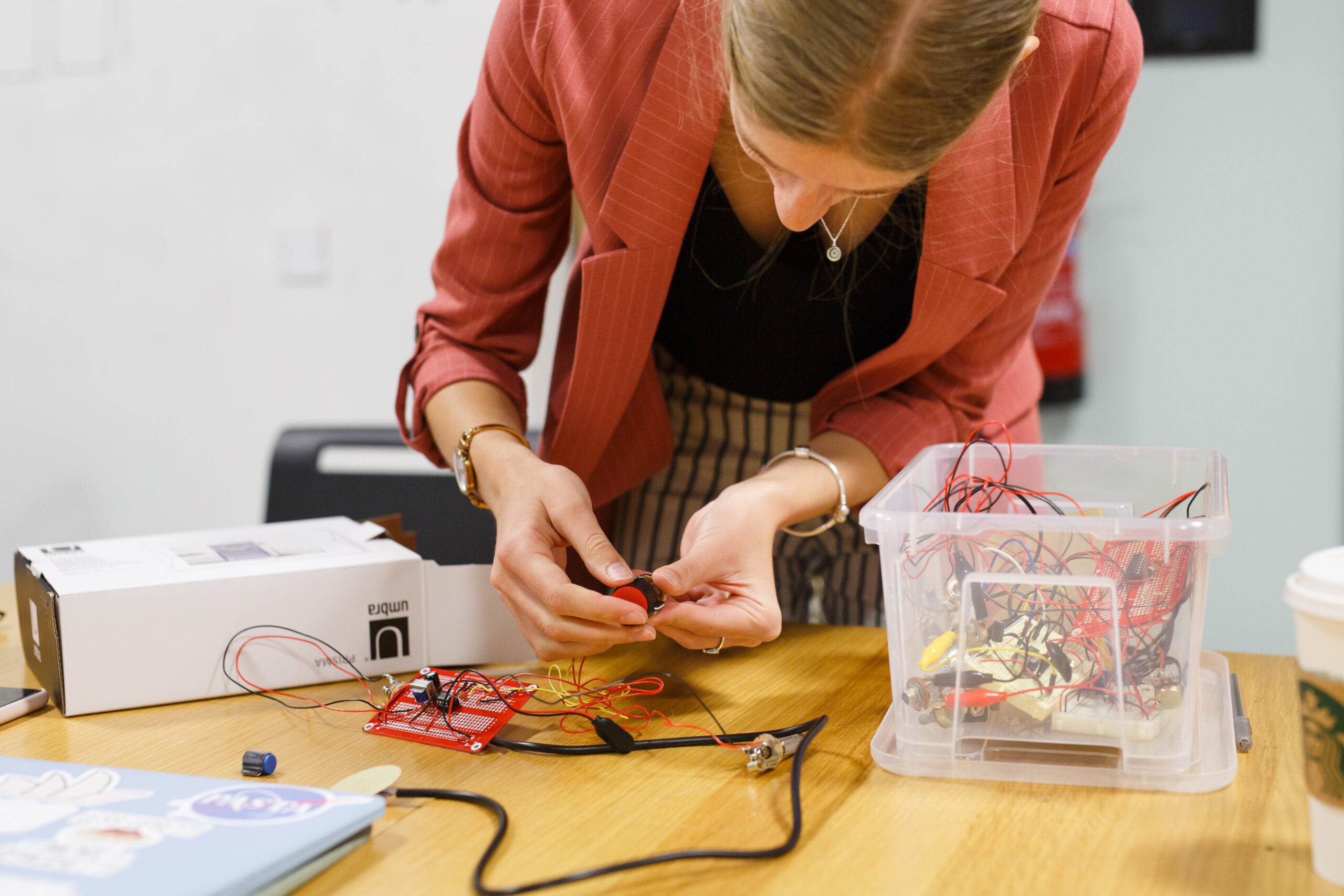 A female-presenting student hunches over a table while working on their robotics project.