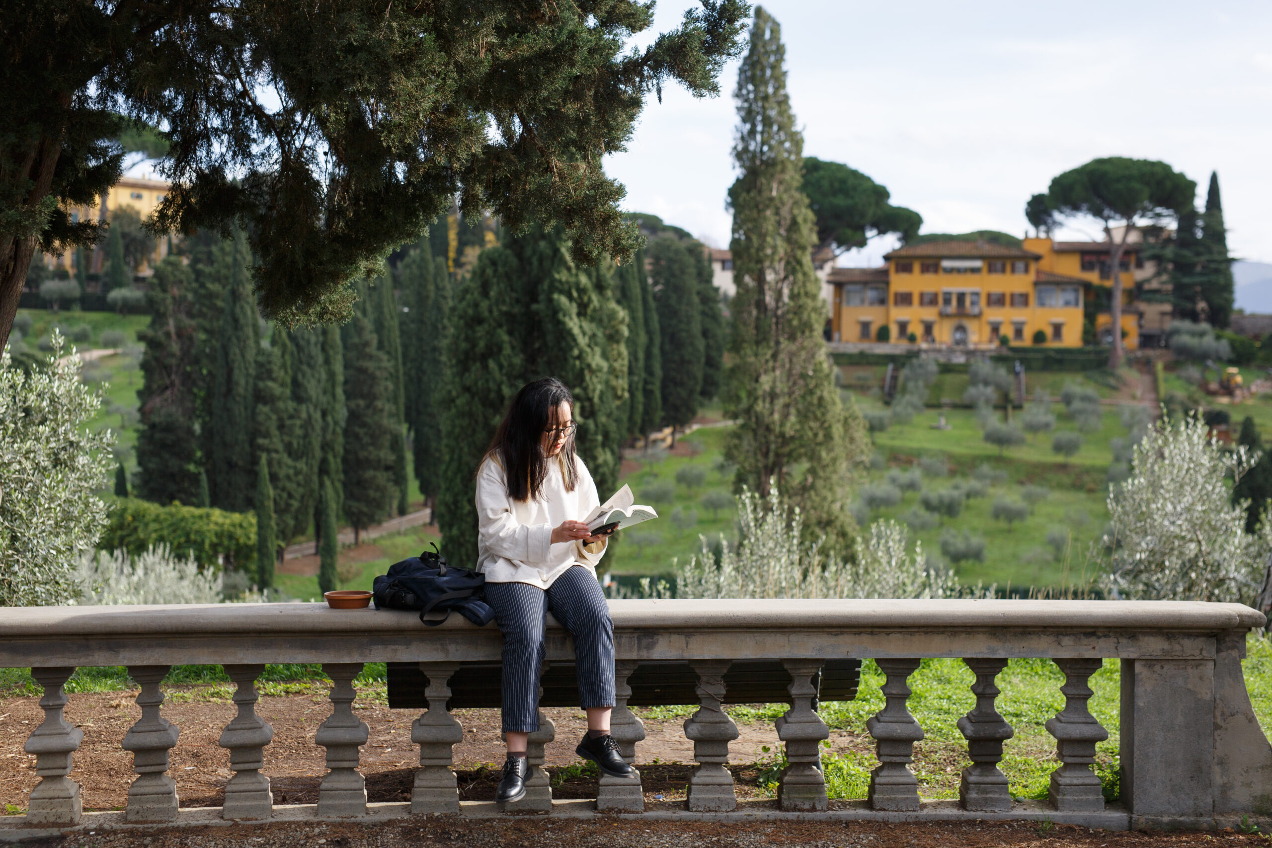 A female-presenting student sits on a stone wall, reading a book, at NYU Florence.
