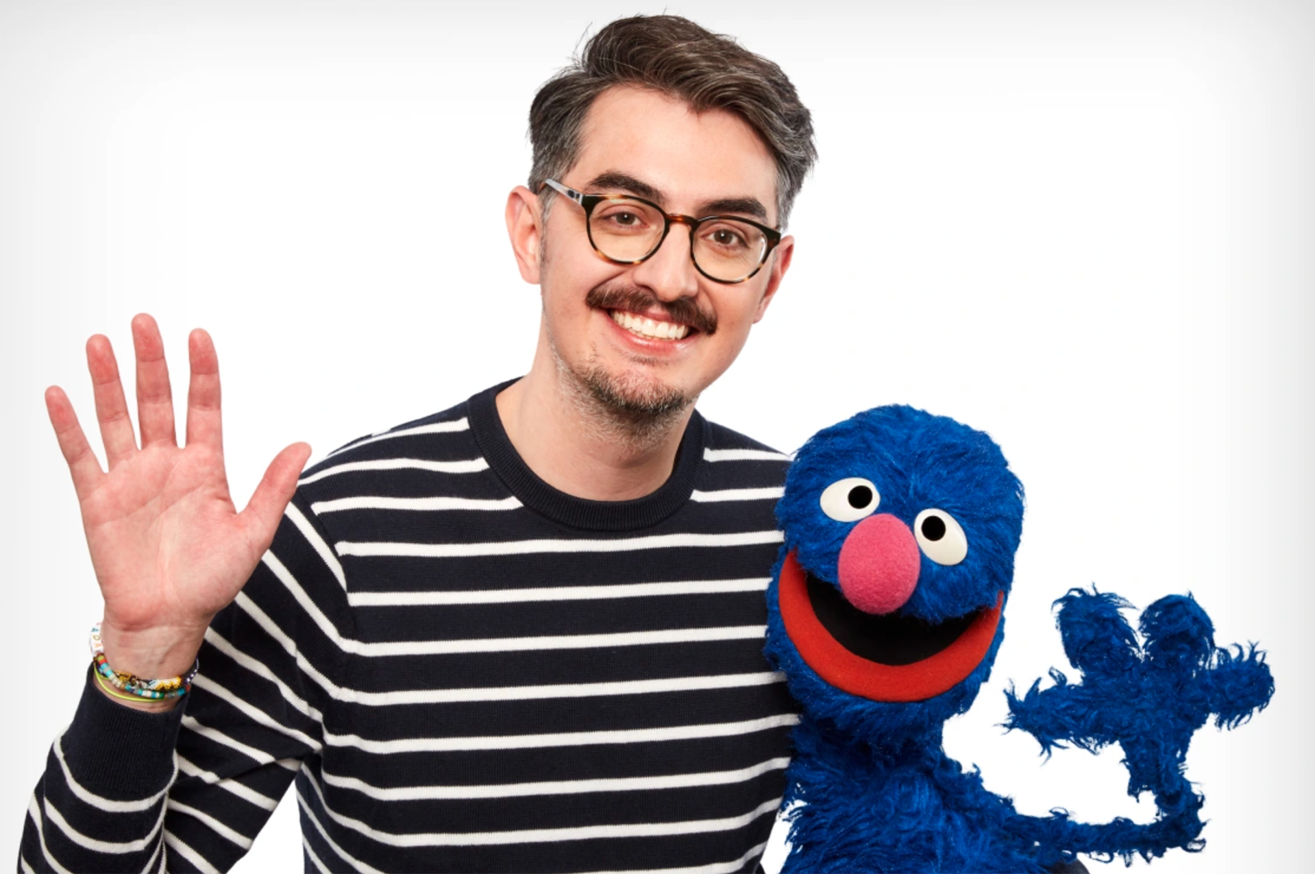 NYU Tisch alum Sal Perez waves his hand while standing next to Grover, a blue puppet character who appears on “Sesame Street,” a long-standing television show for children.