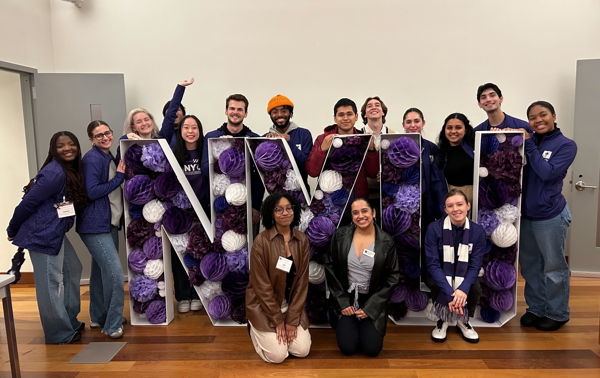A group of Admissions Ambassadors pose in front of large “NYU” letters filled with purple pom-poms.