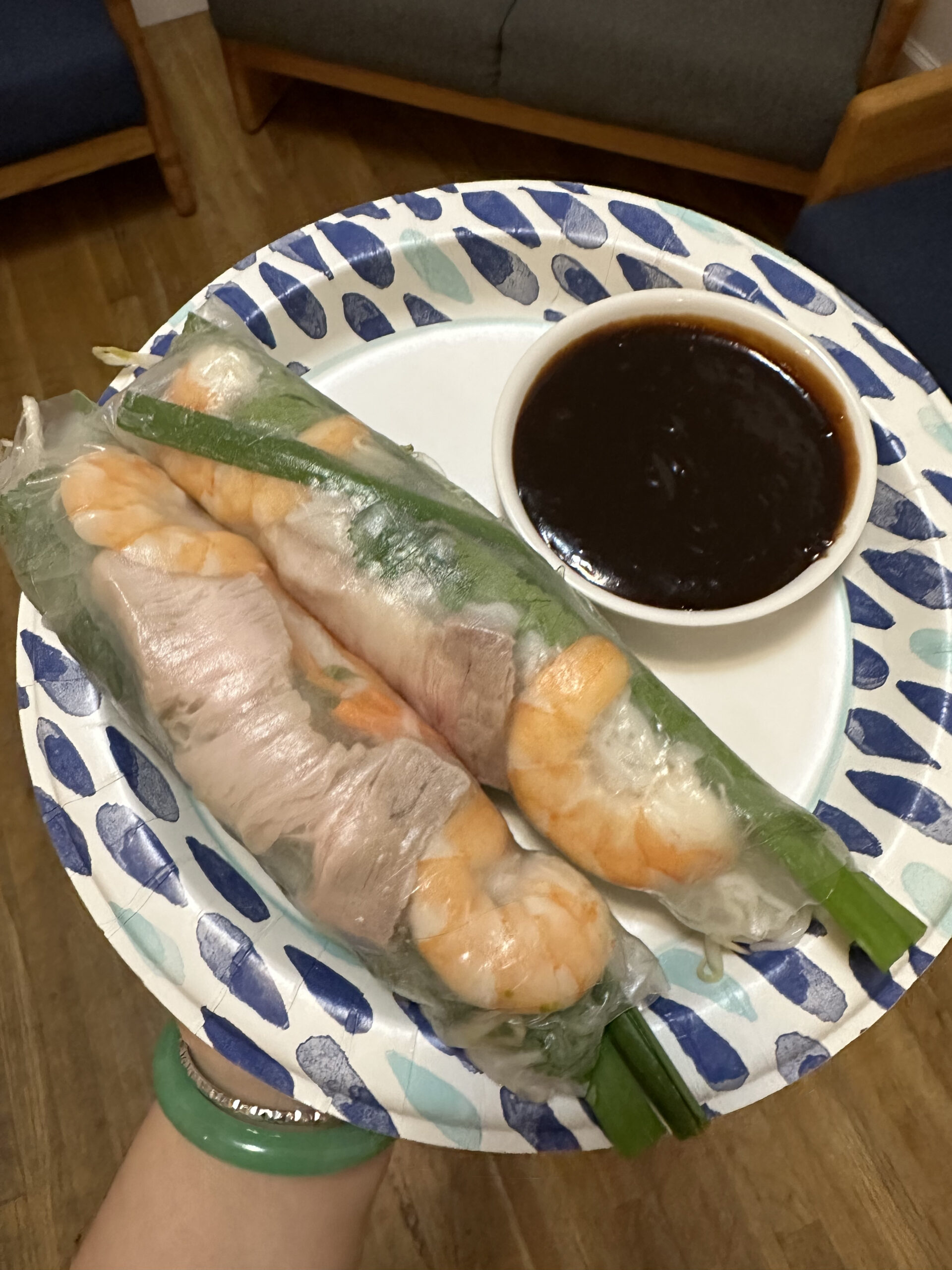 Two summer rolls on a plate next to a small bowl of hoisin sauce.