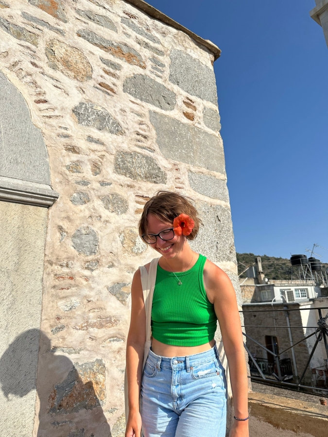 The author wearing a green tank top and pants in Chios, Greece, while studying away. They have a flower tucked behind their ear.