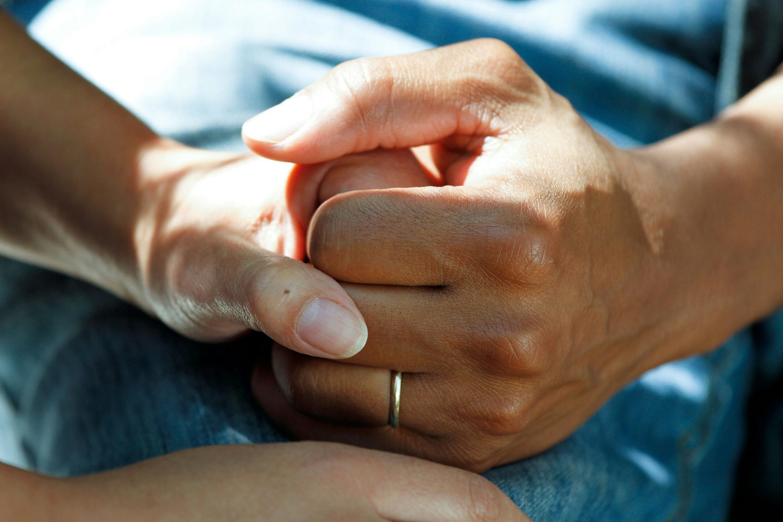 Two individuals clasping hands. One hand has a wedding band.