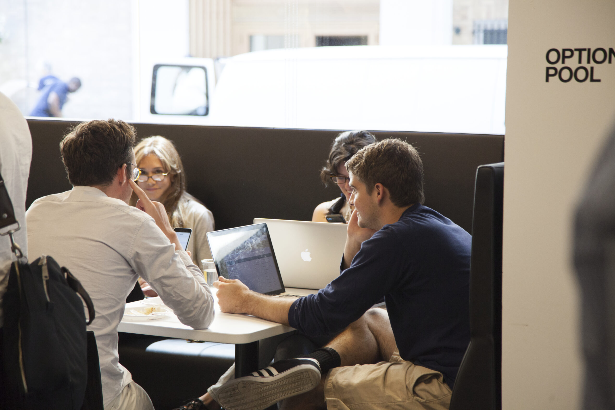 A group of students seated around a table, each working on their devices.