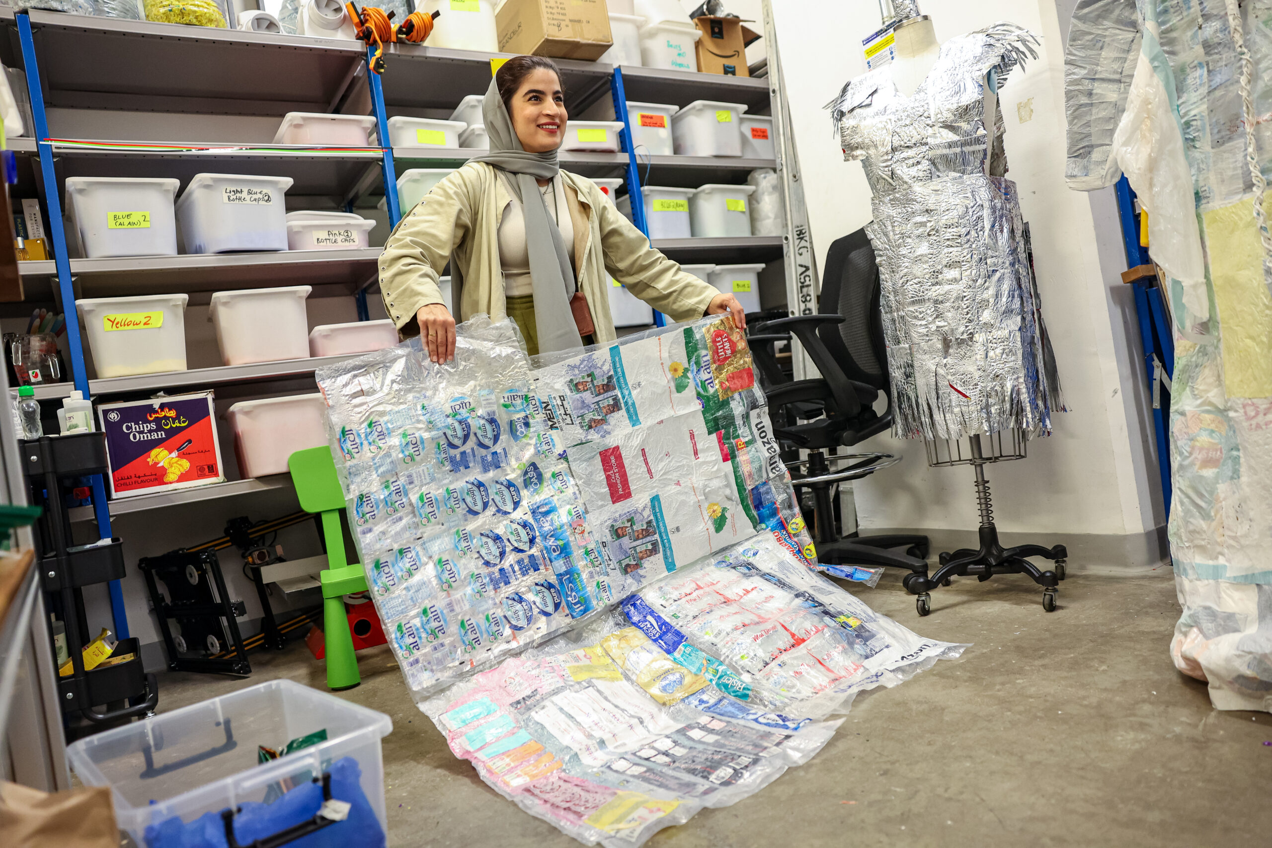 A female-presenting student holding a quilt made out of various recycled plastics.