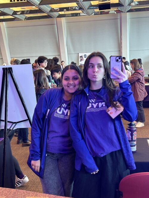 Two students in purple taking a mirror selfie