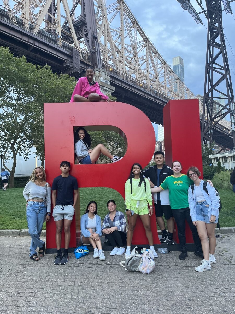 The author and her Project OutReach team posing around large red block letters that spell “RI.” In the background, there is a bridge.