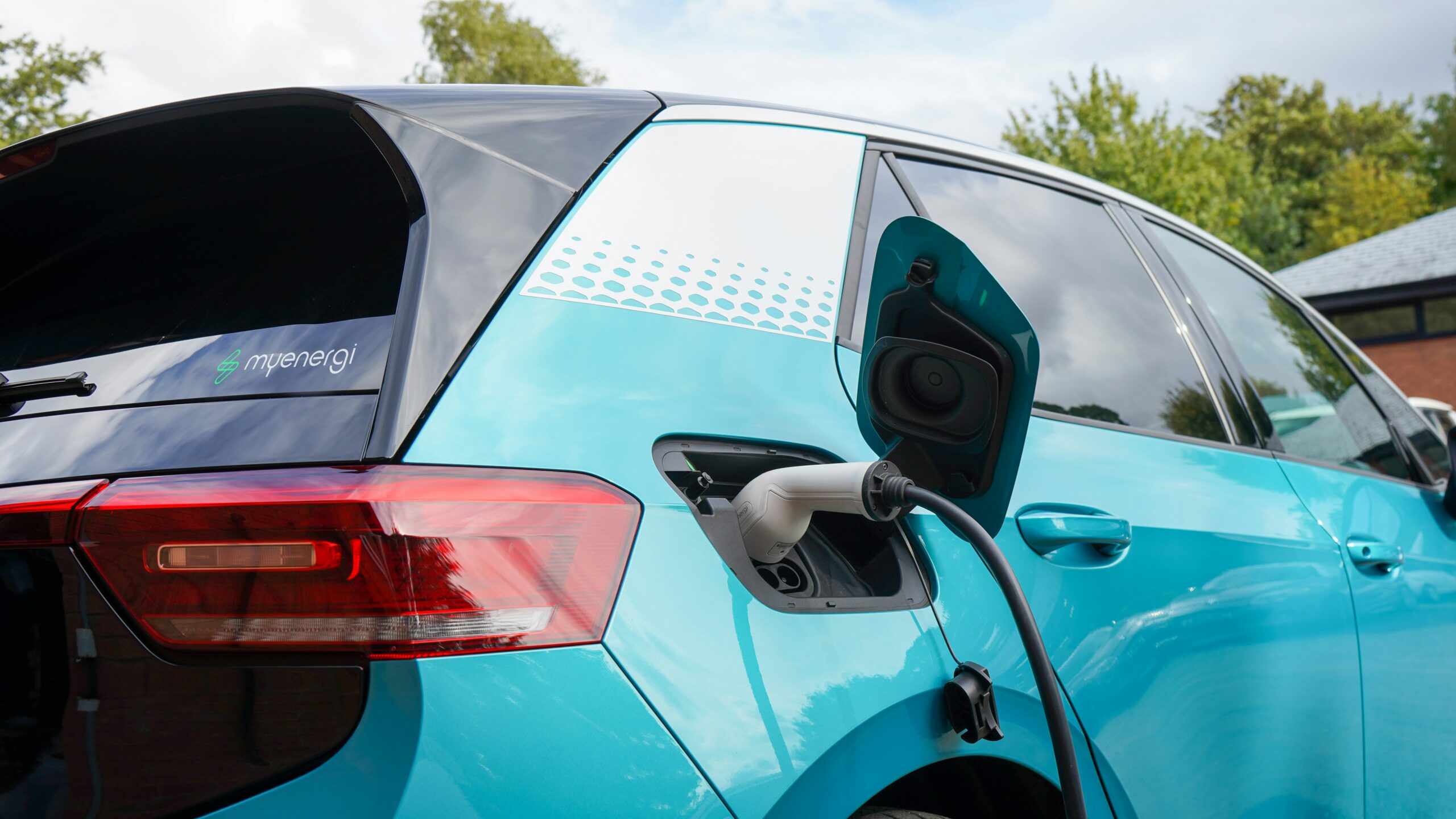 A teal electric car plugged into a charging station.