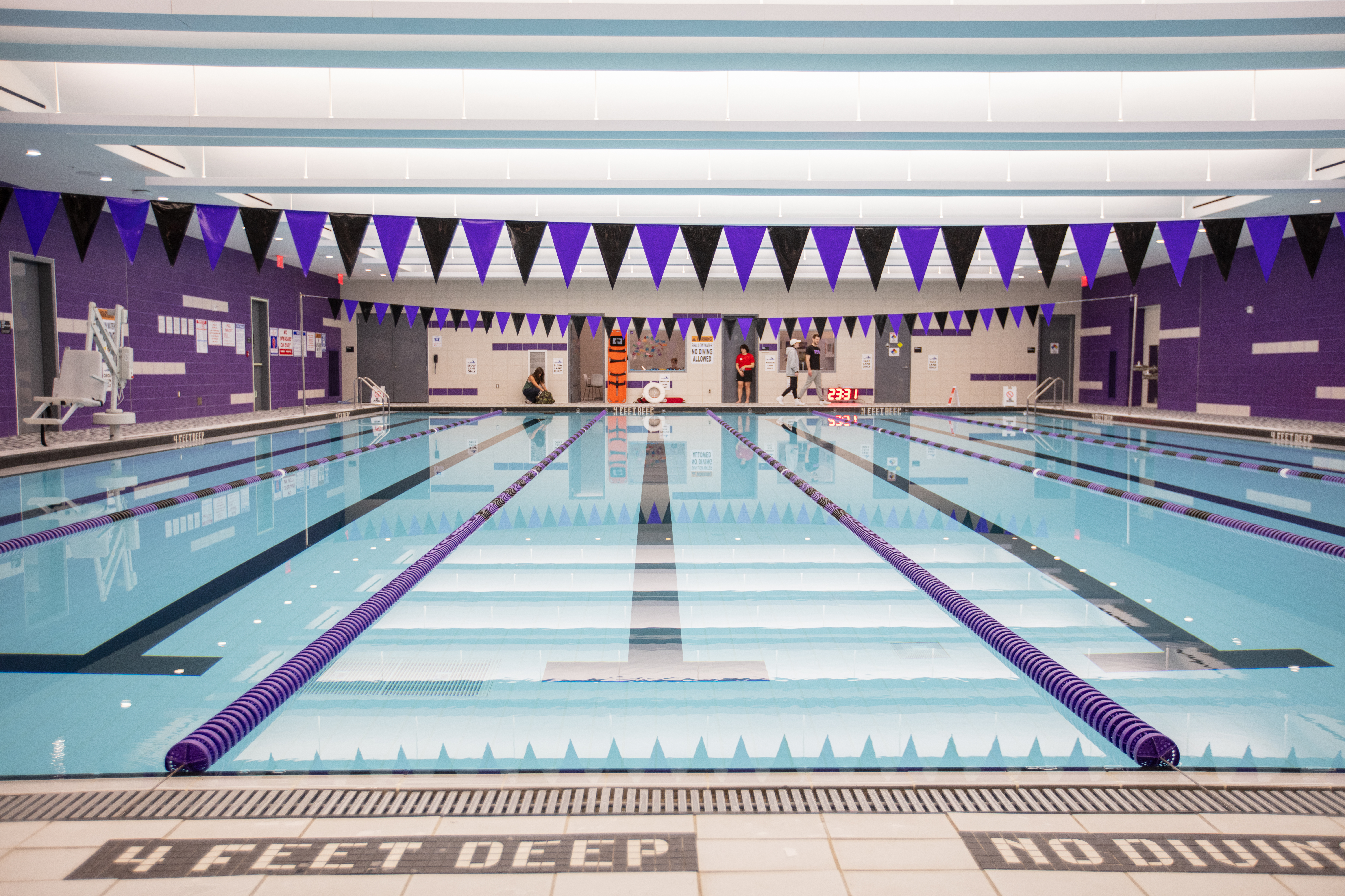 An indoor swimming pool with multiple lanes is ready for use, adorned with purple and black triangular flags hanging above.